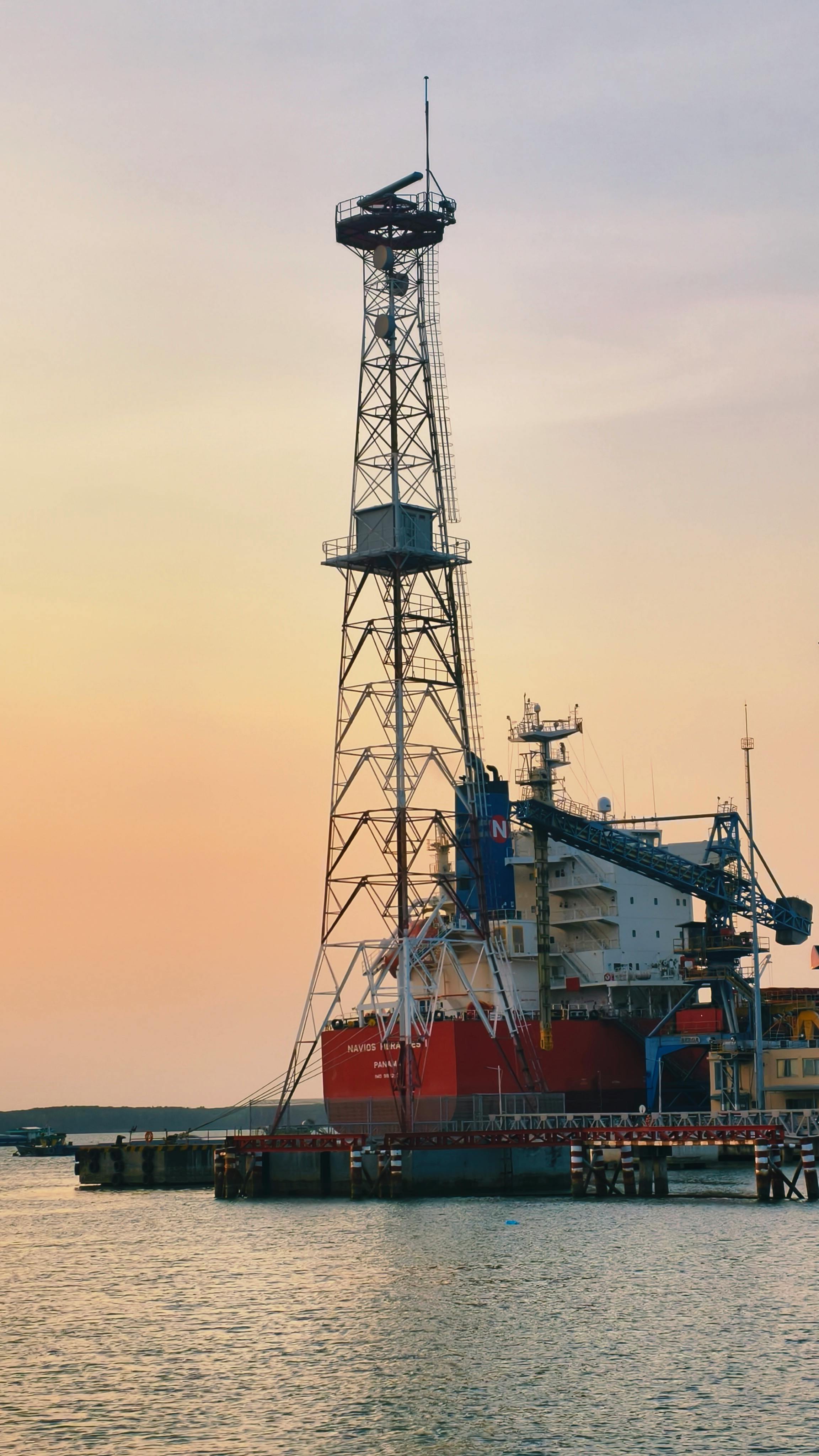 無料 港の鮮やかな夕焼けの中に、そびえ立つ沖合掘削リグが堂々とそびえ立っています。 写真素材