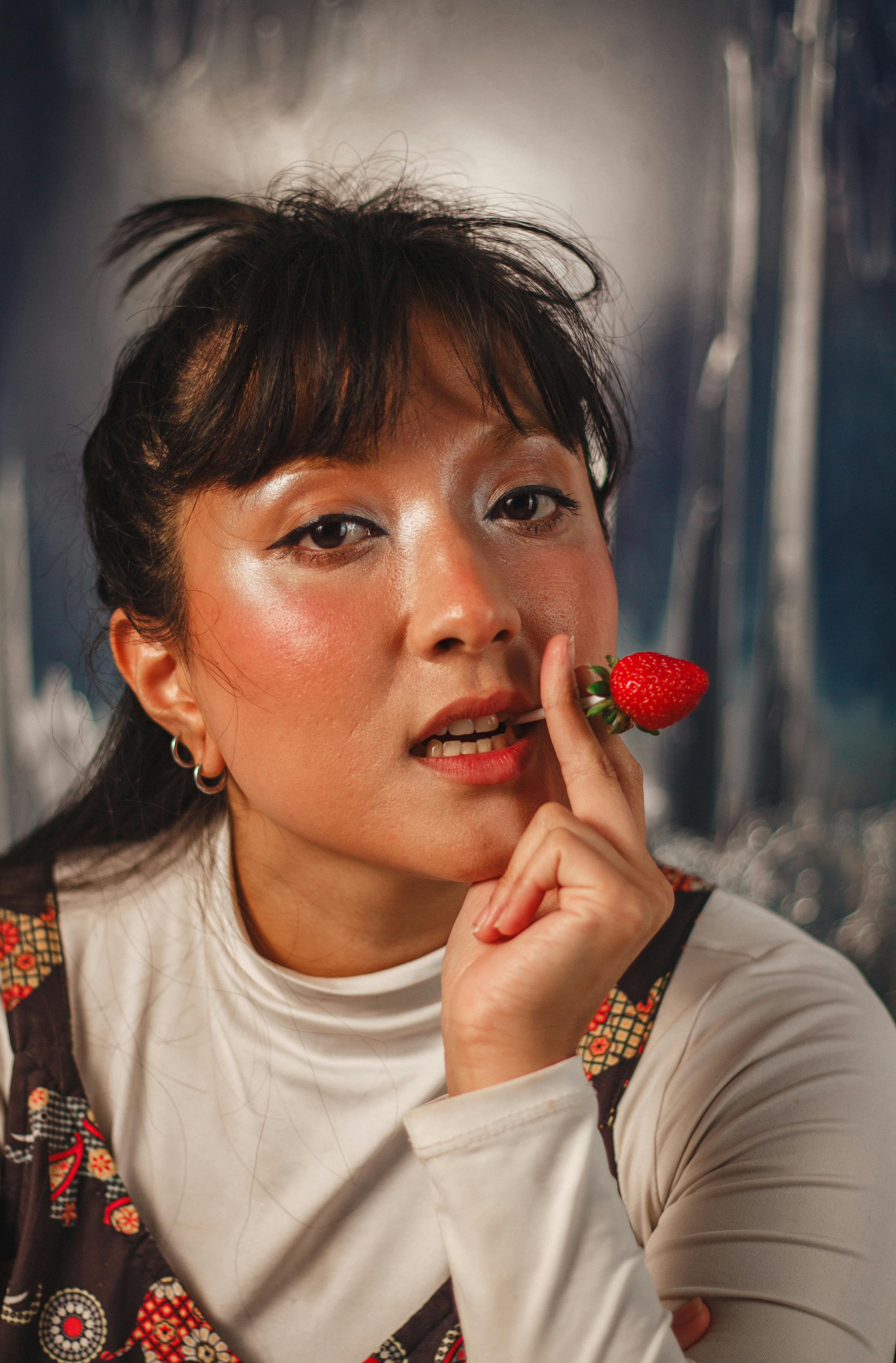 無料 抽象的な背景に、唇の近くにイチゴを持っているアジア人女性の肖像画。 写真素材