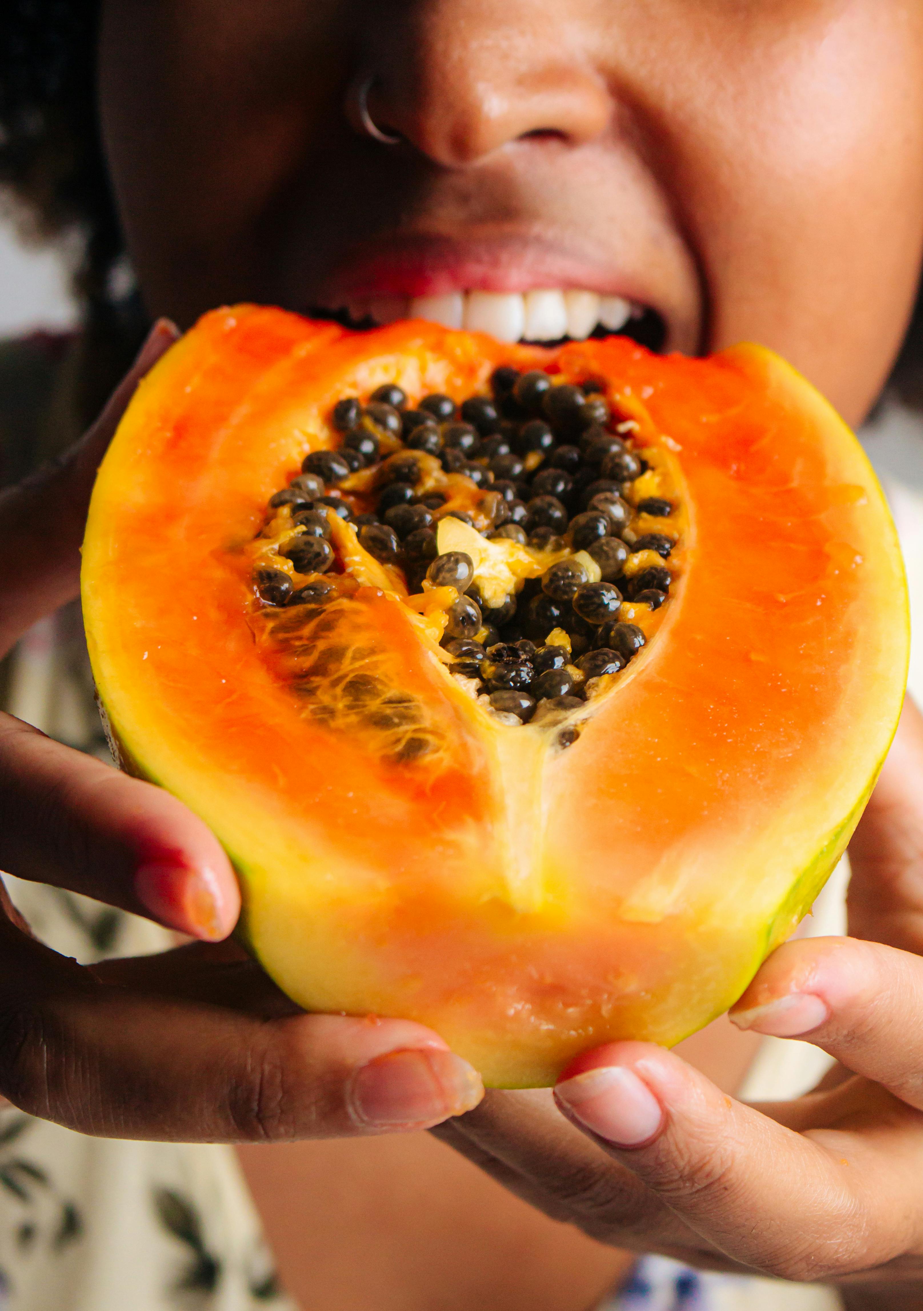 A woman tasting a juicy papaya slice, showcasing vibrant fruit detail.