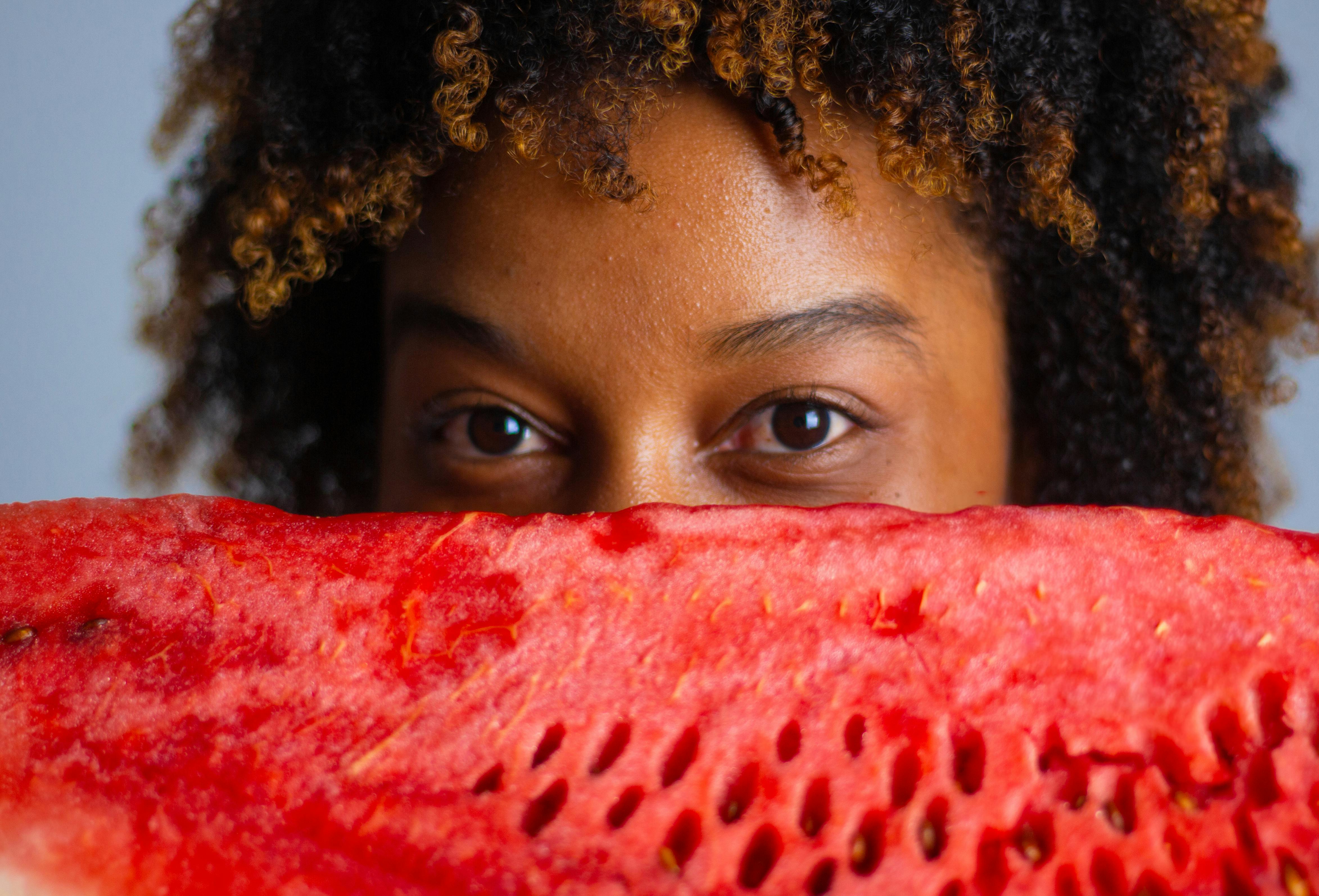 Young woman holding a slice of watermelon near her face, showcasing fresh summer vibe.