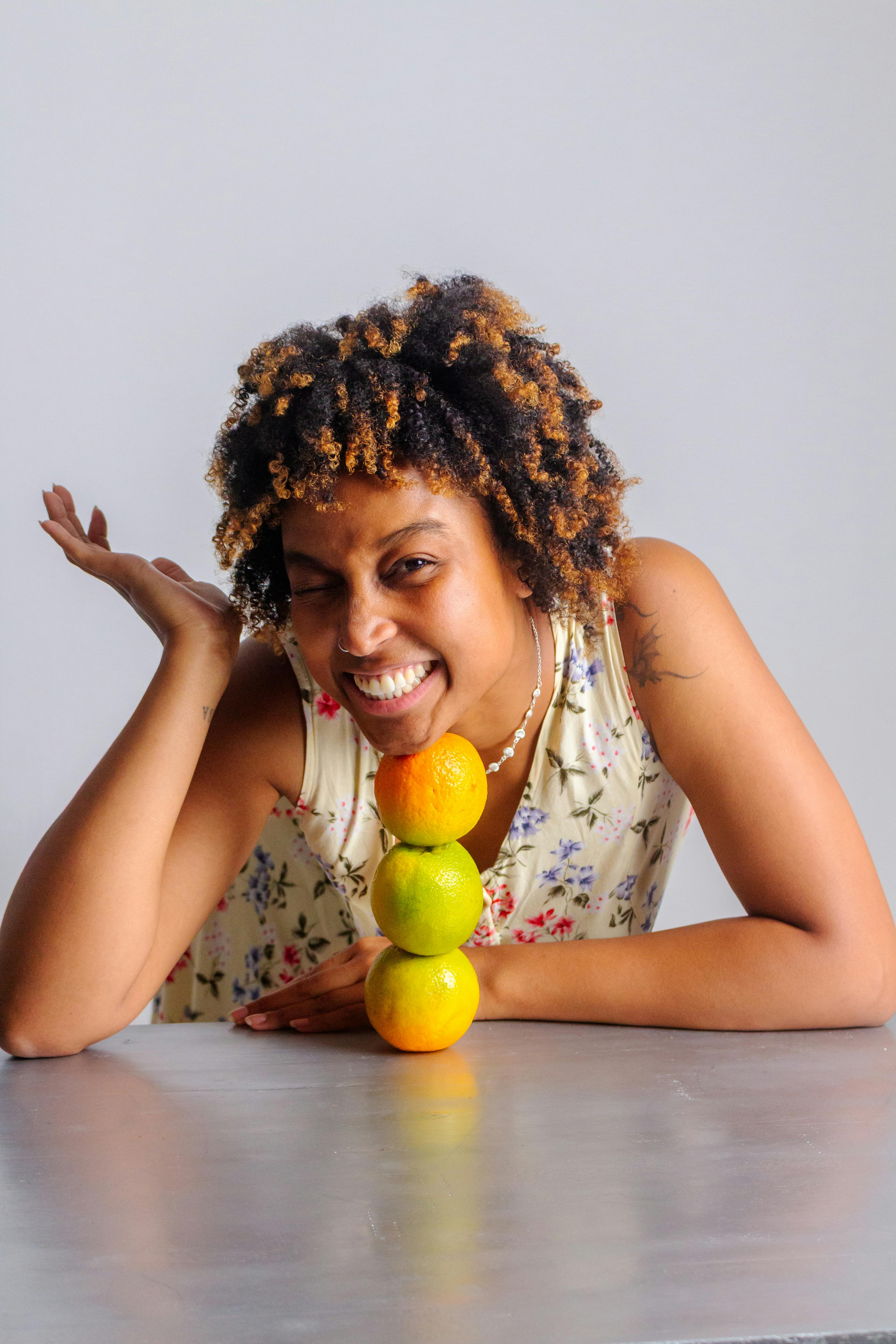 無料 室内で、灰色の表面に柑橘類の果物を積み重ねて微笑む女性。 写真素材