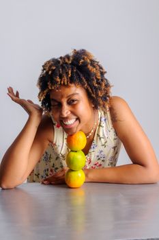 Smiling woman with citrus fruits stacked on a gray surface, indoors.
