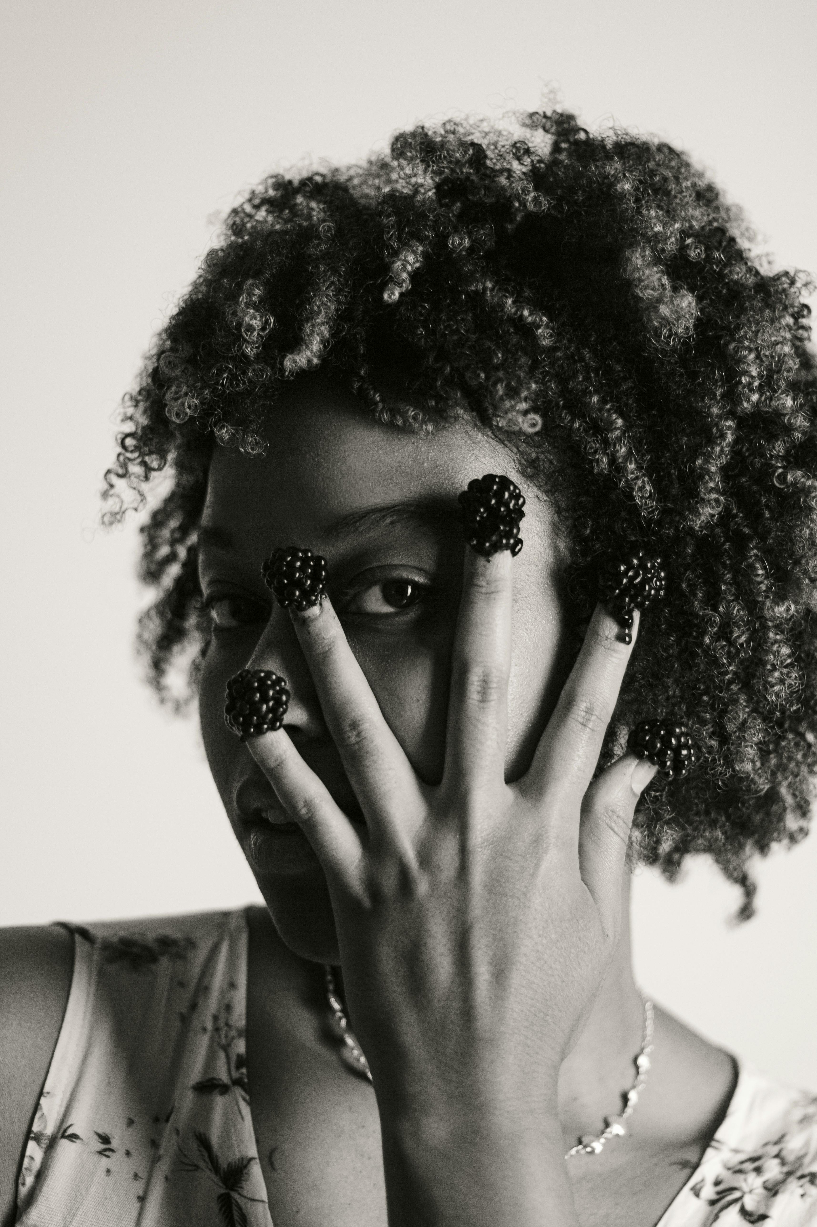 Free Artistic black and white portrait of a woman with blackberries on her fingers, creative expression. Stock Photo