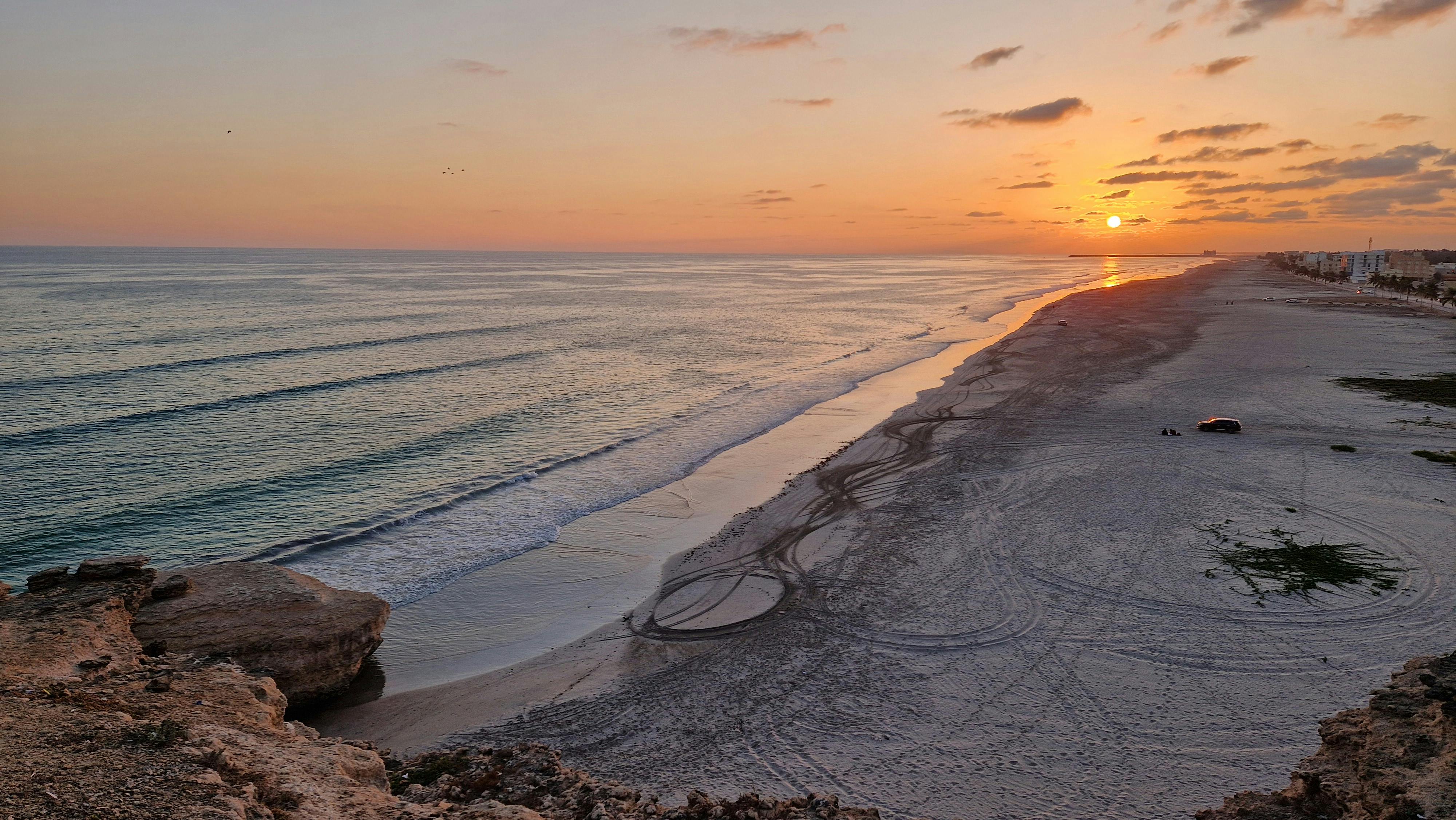Gratis Pemandangan matahari terbenam yang damai di atas pantai yang tenang dengan ombak yang lembut dan langit yang cerah. Foto Stok