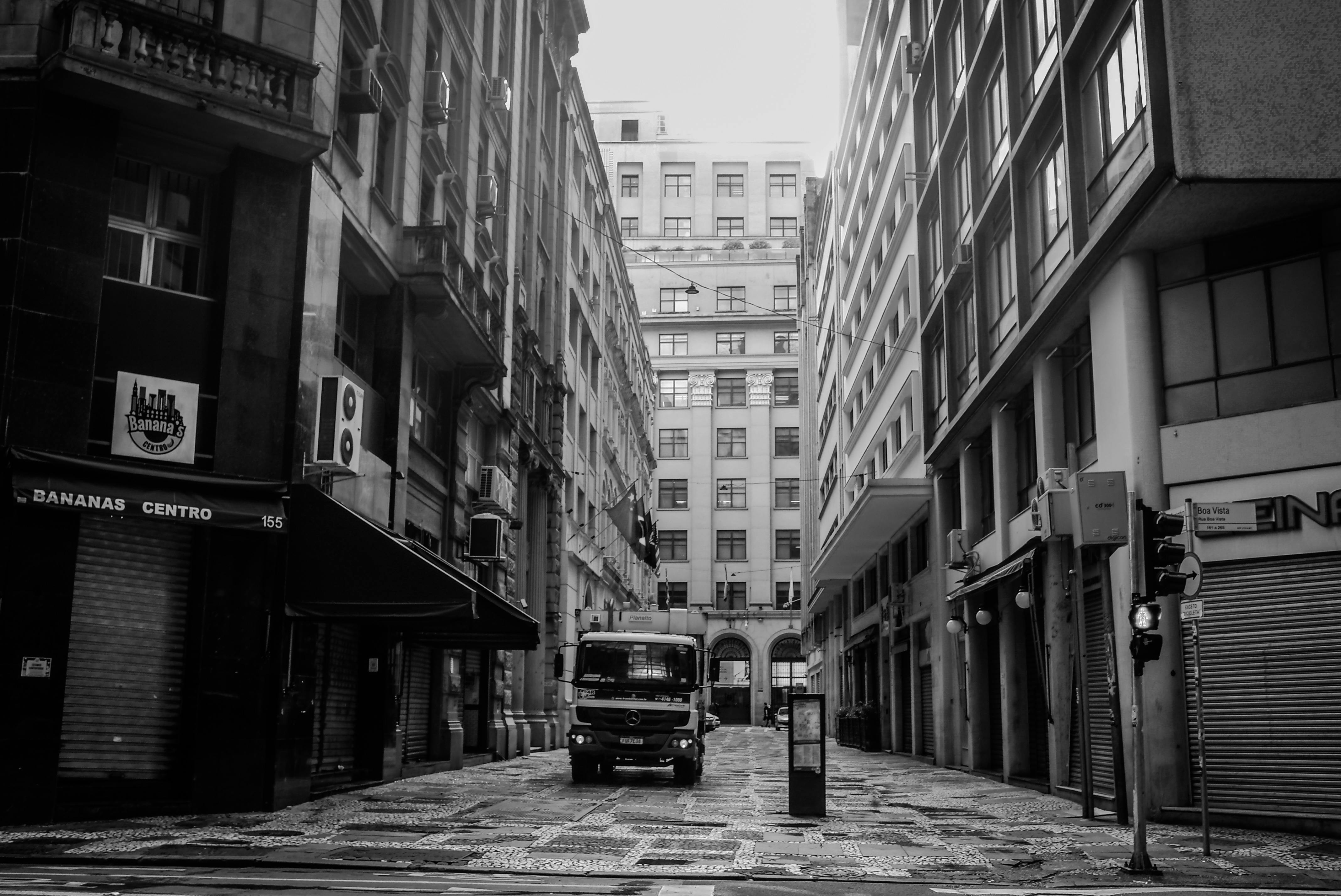 Free Monochrome view of an urban street with a parked truck between tall buildings. Stock Photo