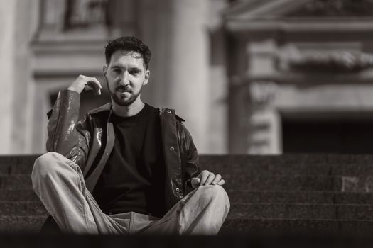 Stylish black and white portrait of a man sitting outdoors, expressing deep thought.