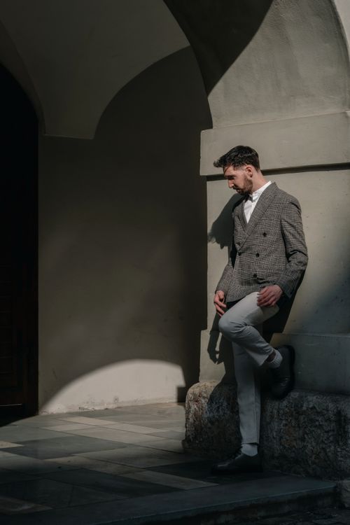 Free Man in sophisticated modern outfit leaning against a stone archway in sunlight. Stock Photo