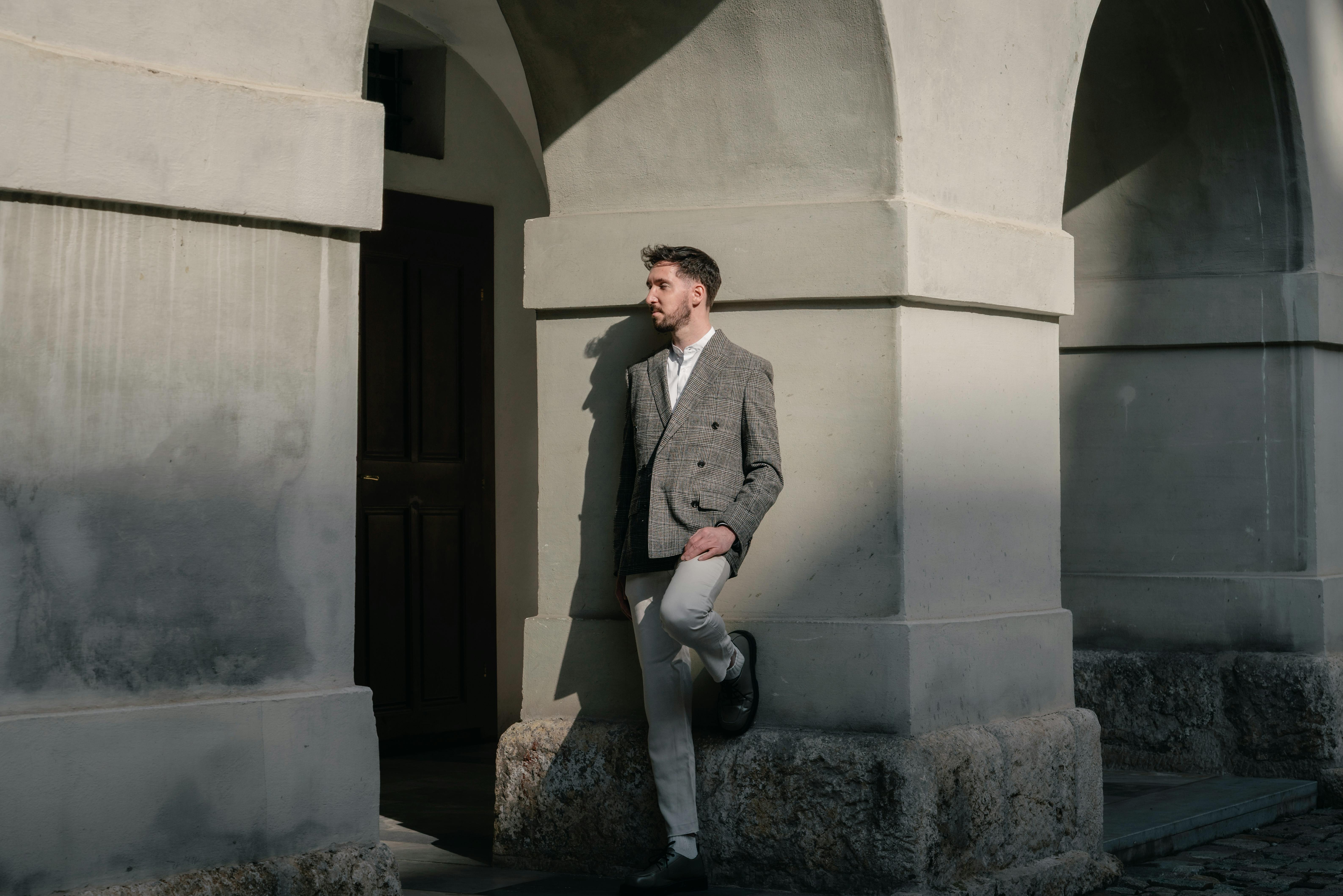 無料 おしゃれな男性がアーチ型の建築物を背景にポーズをとり、都会的な優雅さを表現しています。 写真素材