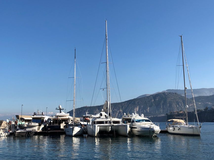 Spectacular Private Luxury Yacht Tour of Capri from Rome by Train Review 2026 - A scenic view of luxury yachts docked at a marina with mountains in the background under a clear blue sky.