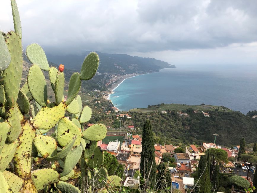 Dramatic coastal view of Taormina, Sicily with prickly pear cactus in the foreground.