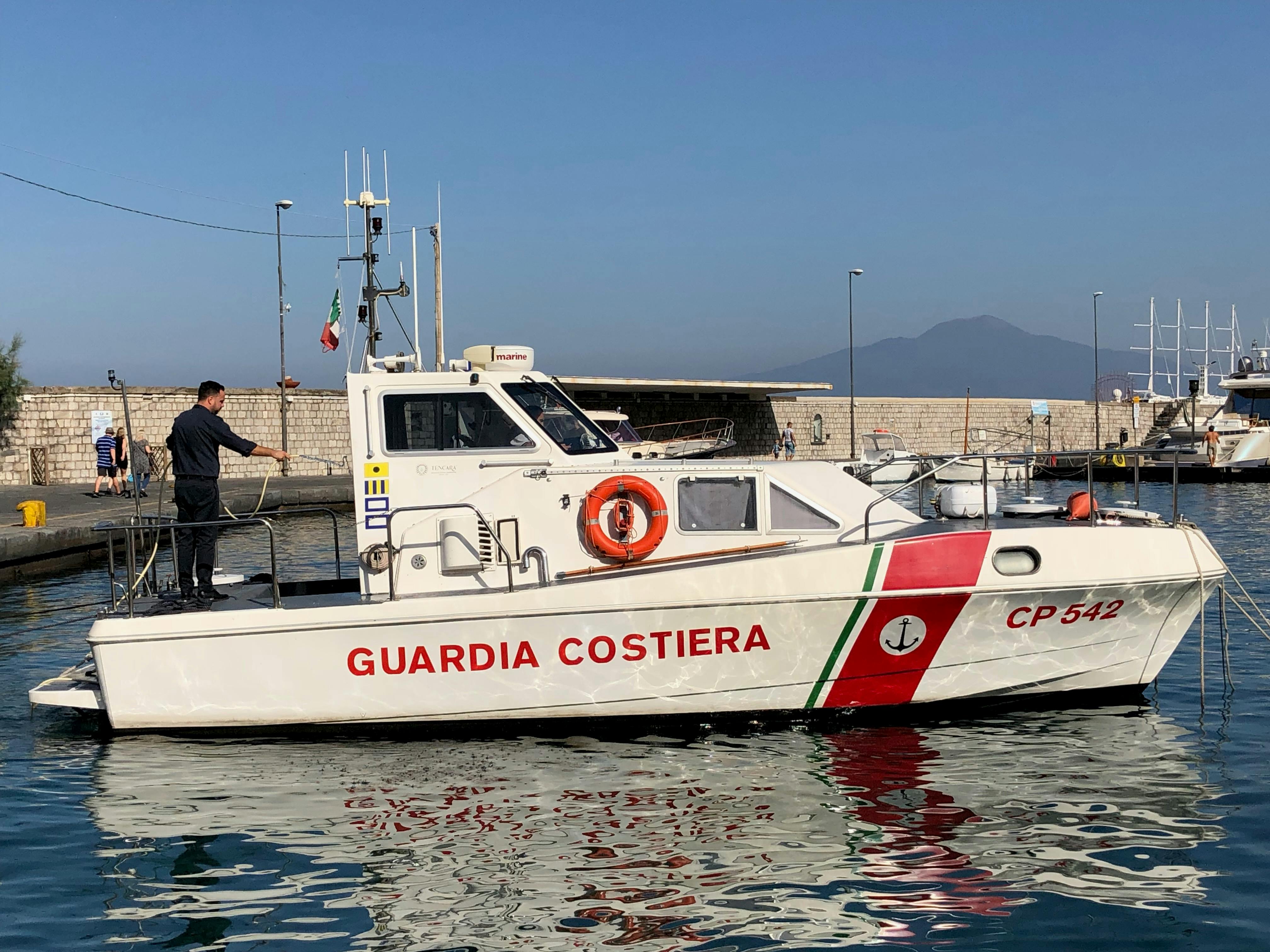 無料 晴れた日に、ベスビオ山を背景に停泊しているイタリア沿岸警備隊の船。 写真素材