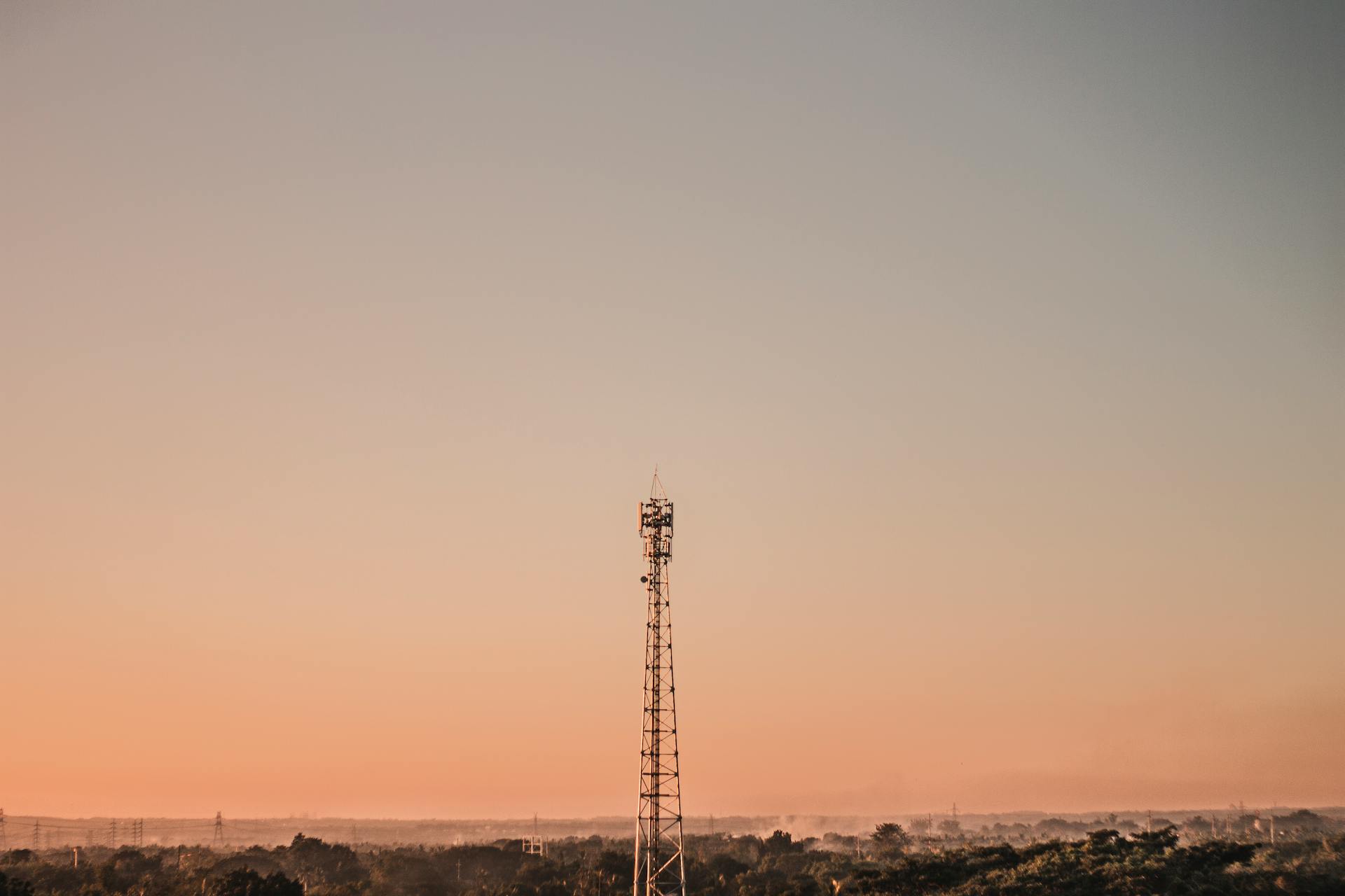 A calm landscape featuring a telecommunication tower against a sunset sky, symbolizing modern connectivity.