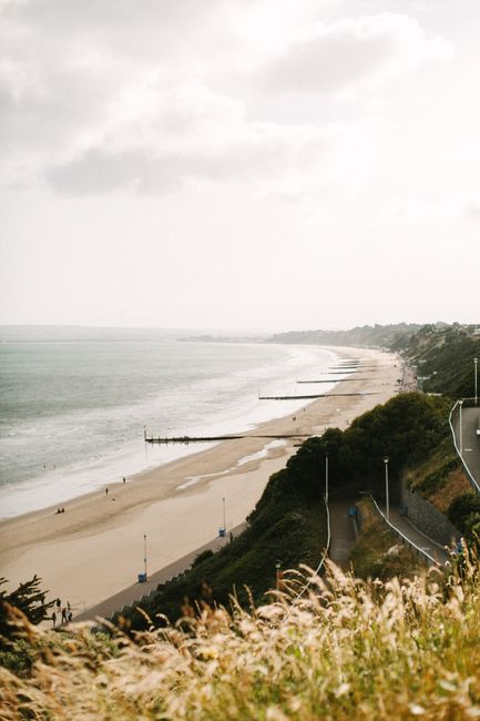 Picturesque scenery of sandy coast and powerful waving ocean surrounded by green hills against cloudy sky