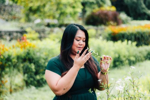 Free A woman in a green dress appreciating flowers in a lush garden setting. Stock Photo