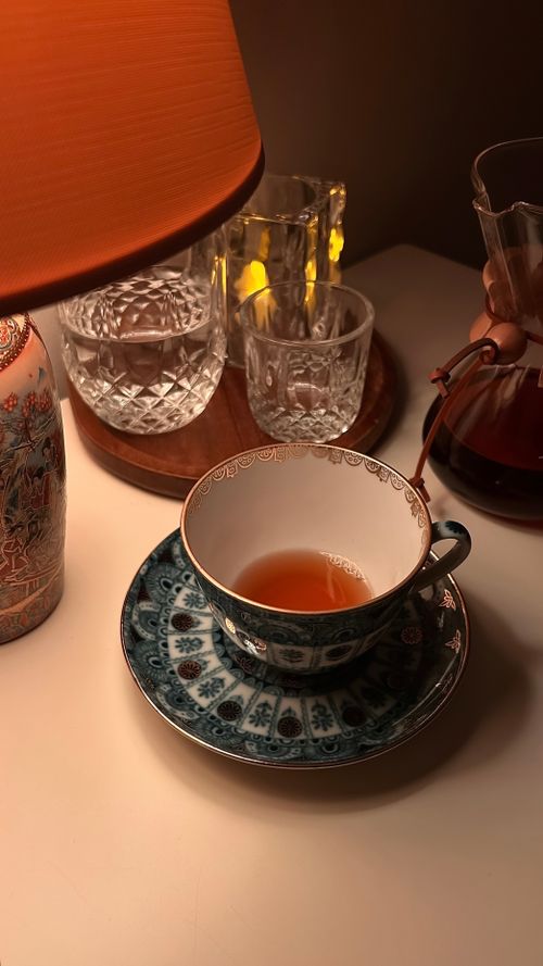 Free Elegant tea scene with intricate cup, warm lamp, and cozy ambiance. Stock Photo