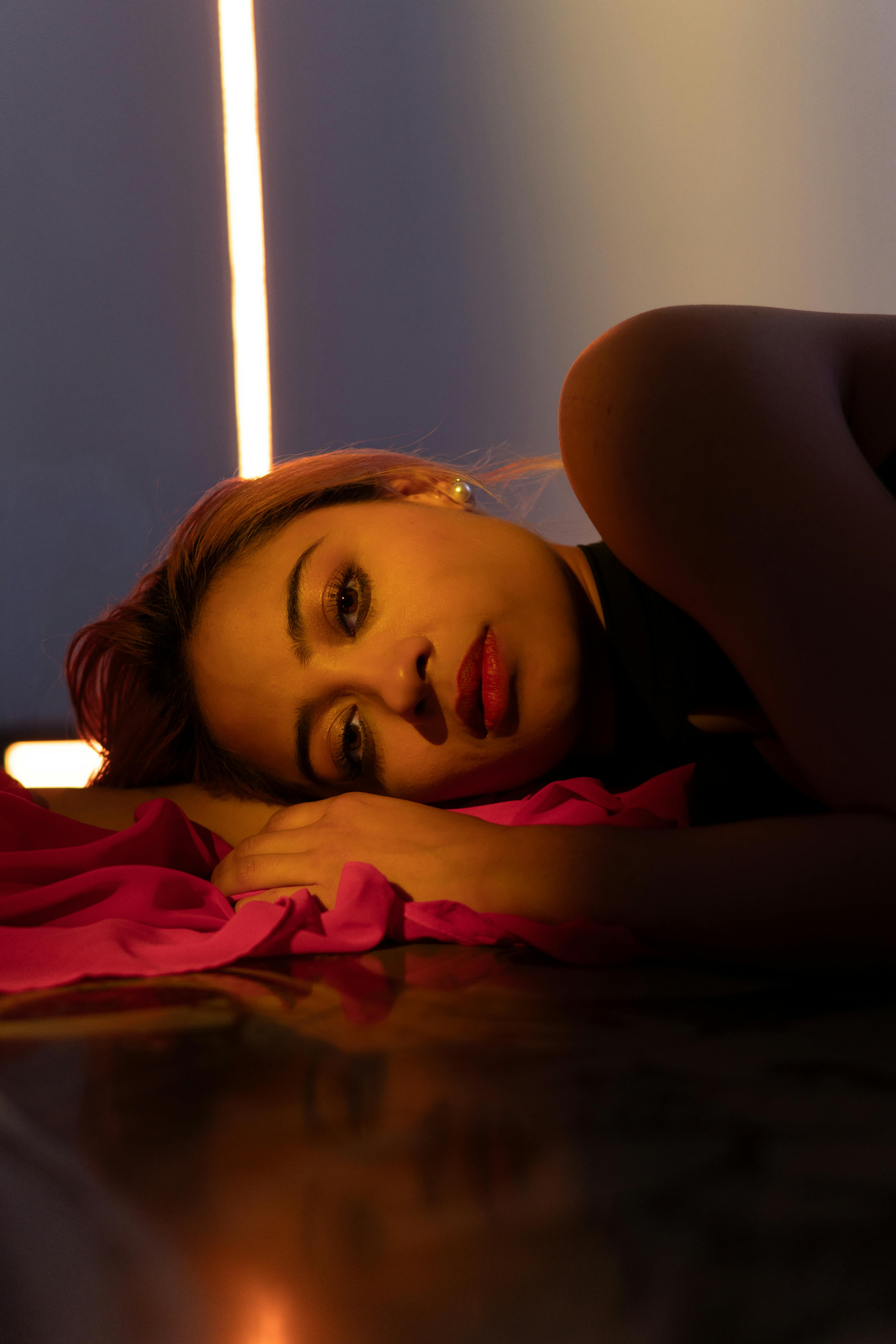 無料 ラテン系の女性がドラマチックな照明、赤い布、赤い口紅をつけた床に横たわり、芸術的な肖像画を作り上げています。 写真素材