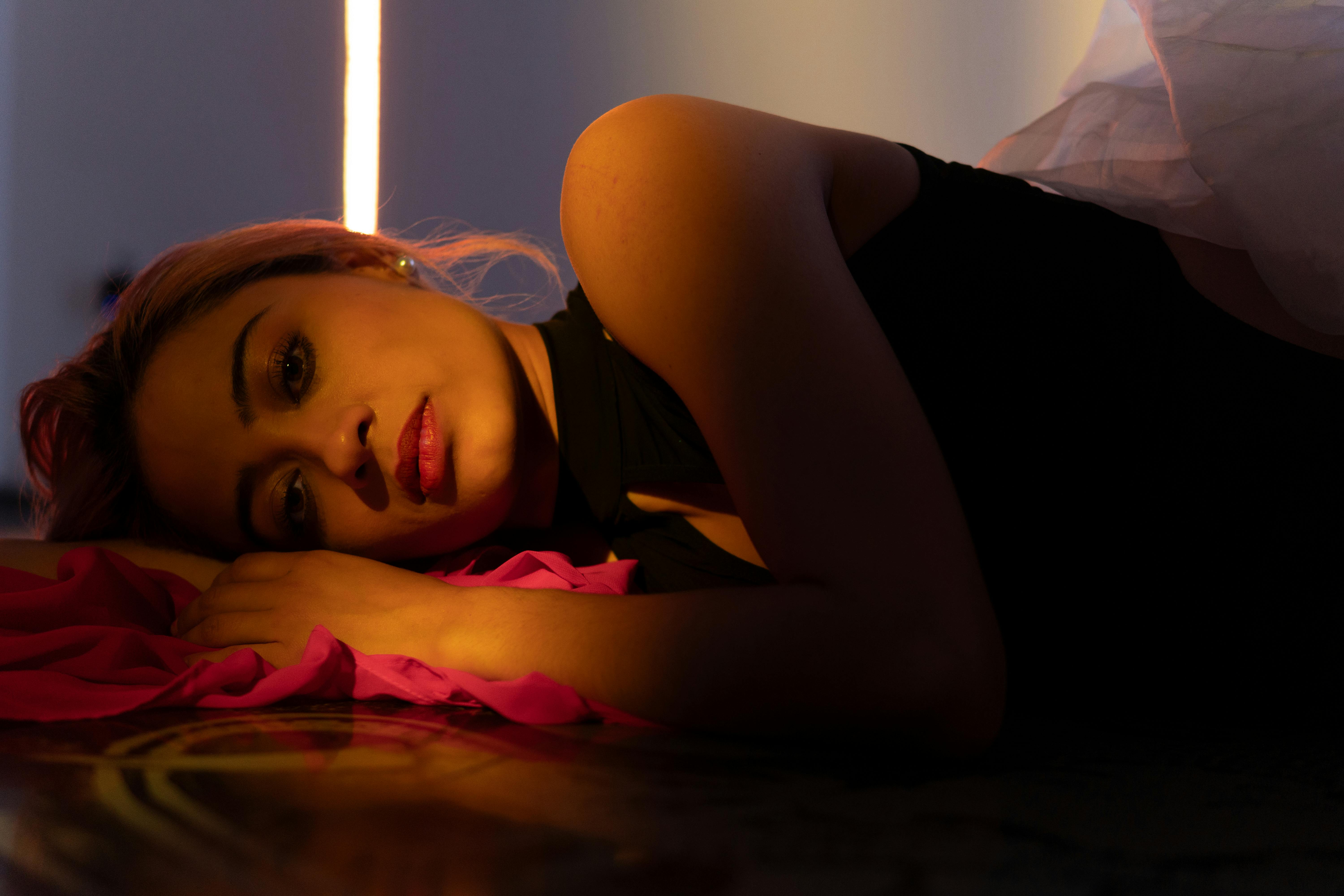 無料 ドラマチックな照明が顔を照らし、床に横たわる女性の陰鬱なポートレート。 写真素材