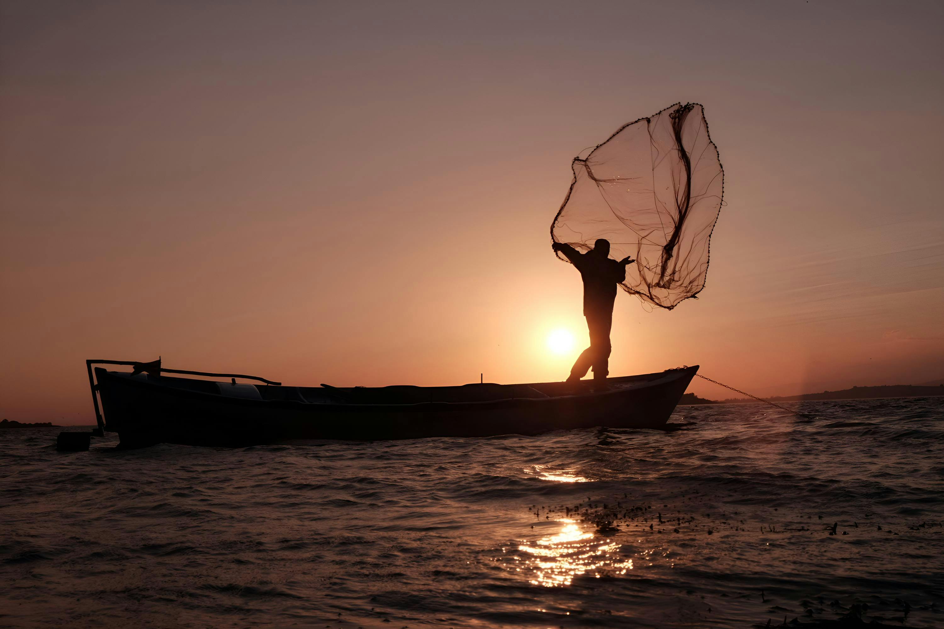 Free Silhouette of fisherman casting net at sunset on a boat in İstanbul waters. Stock Photo