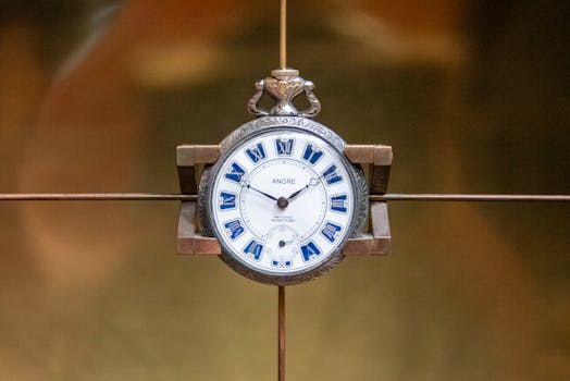 Close-up of an antique pocket watch with blue Roman numerals on a warm background.