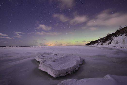 Breathtaking view of the Northern Lights illuminating a frozen coastline in Estonia at night.