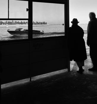 Silhouettes of two people observing a passing boat on Venetian waters through a window.