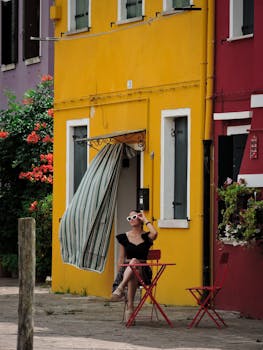 A fashionable woman relaxes in Burano, Venice, with vibrant buildings and summer vibes.