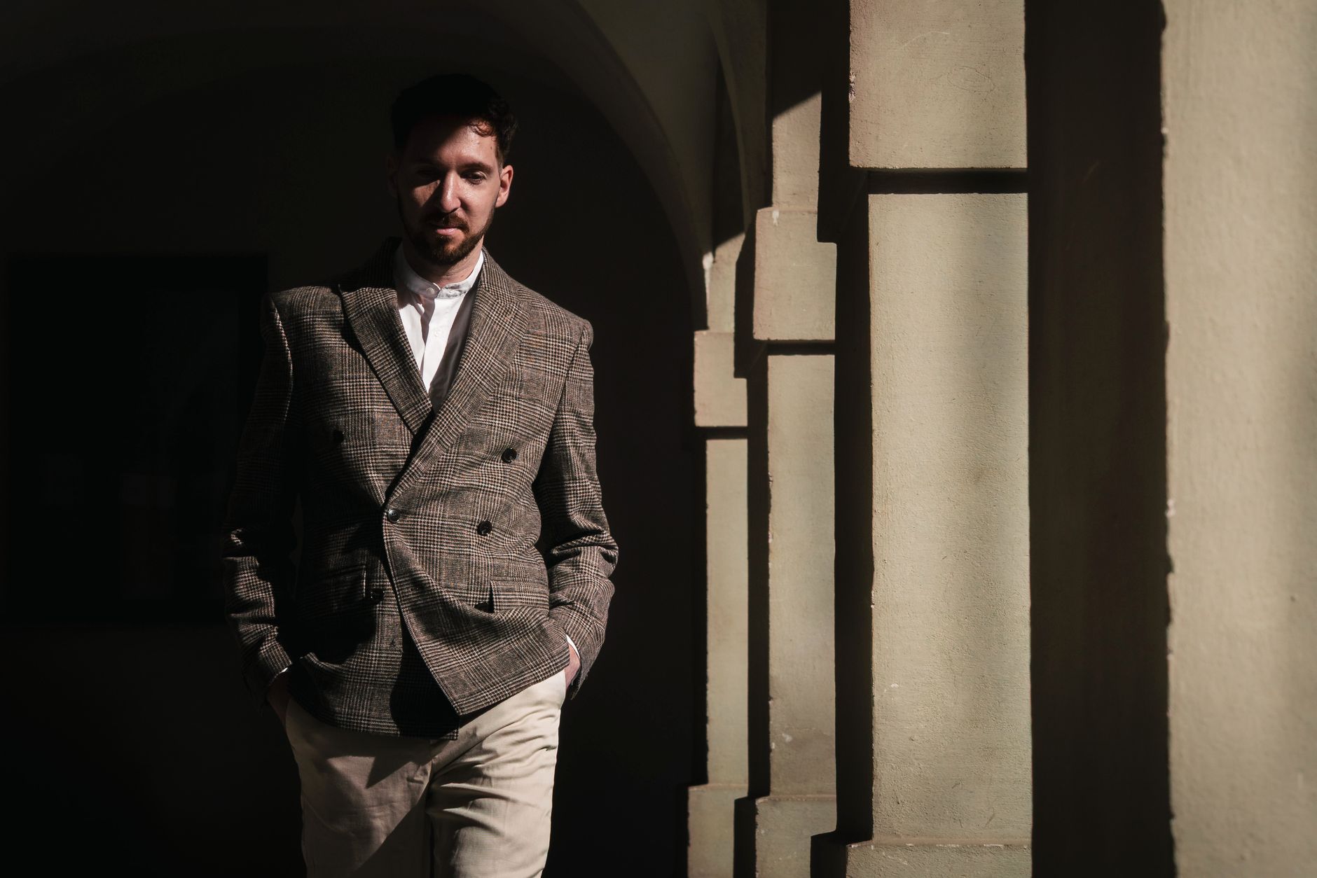 A fashionable man in a modern blazer poses under sunlit archways in Graz, Austria.