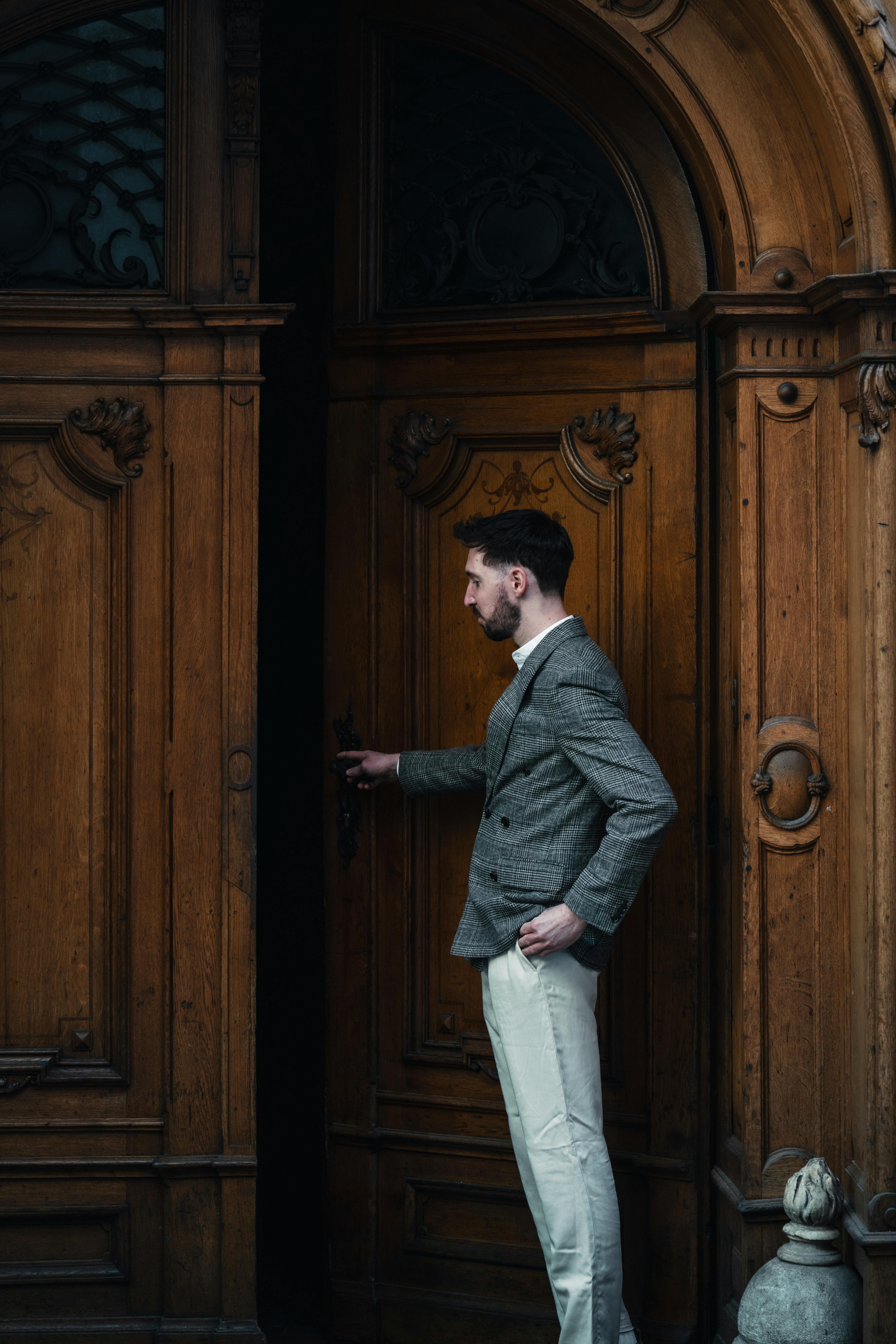 grátis Homem elegante em traje clássico abrindo uma porta de madeira antiga em Graz, Áustria. Foto profissional