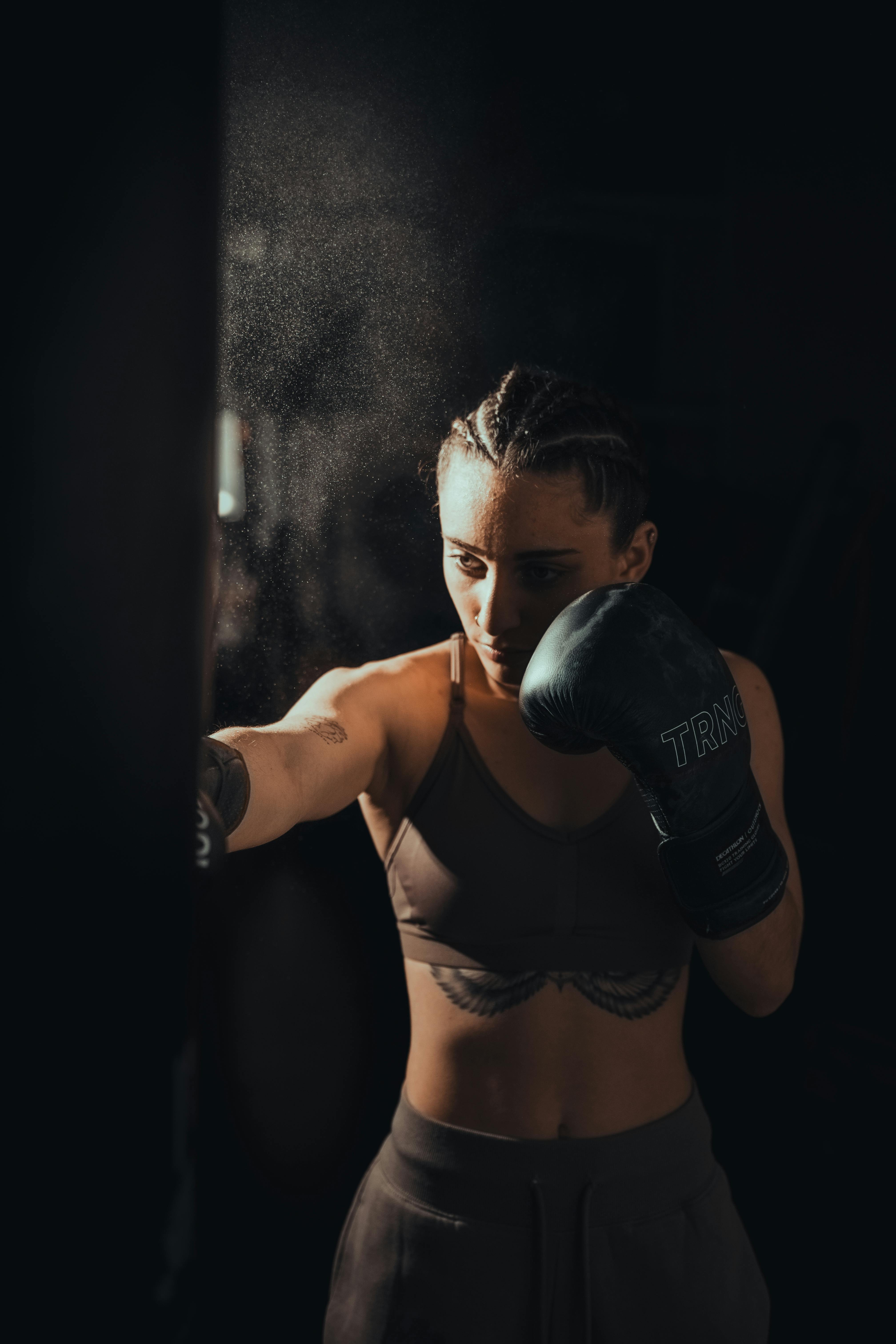 бесплатная Целеустремленная боксерша тренируется в полумраке спортзала, демонстрируя силу и сосредоточенность. Стоковое фото