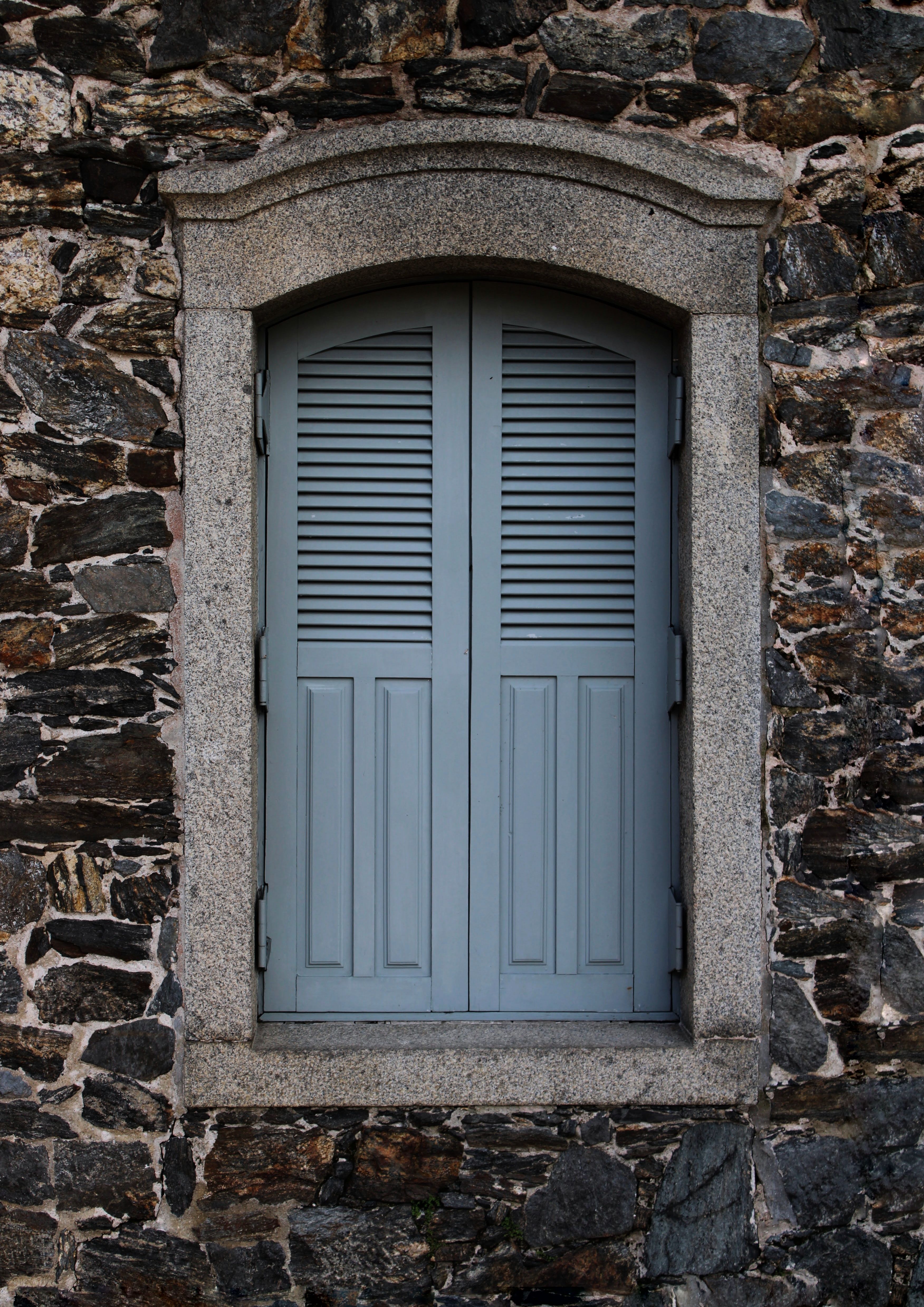 A closed shuttered window set in an old stone wall, conveying classic architecture.
