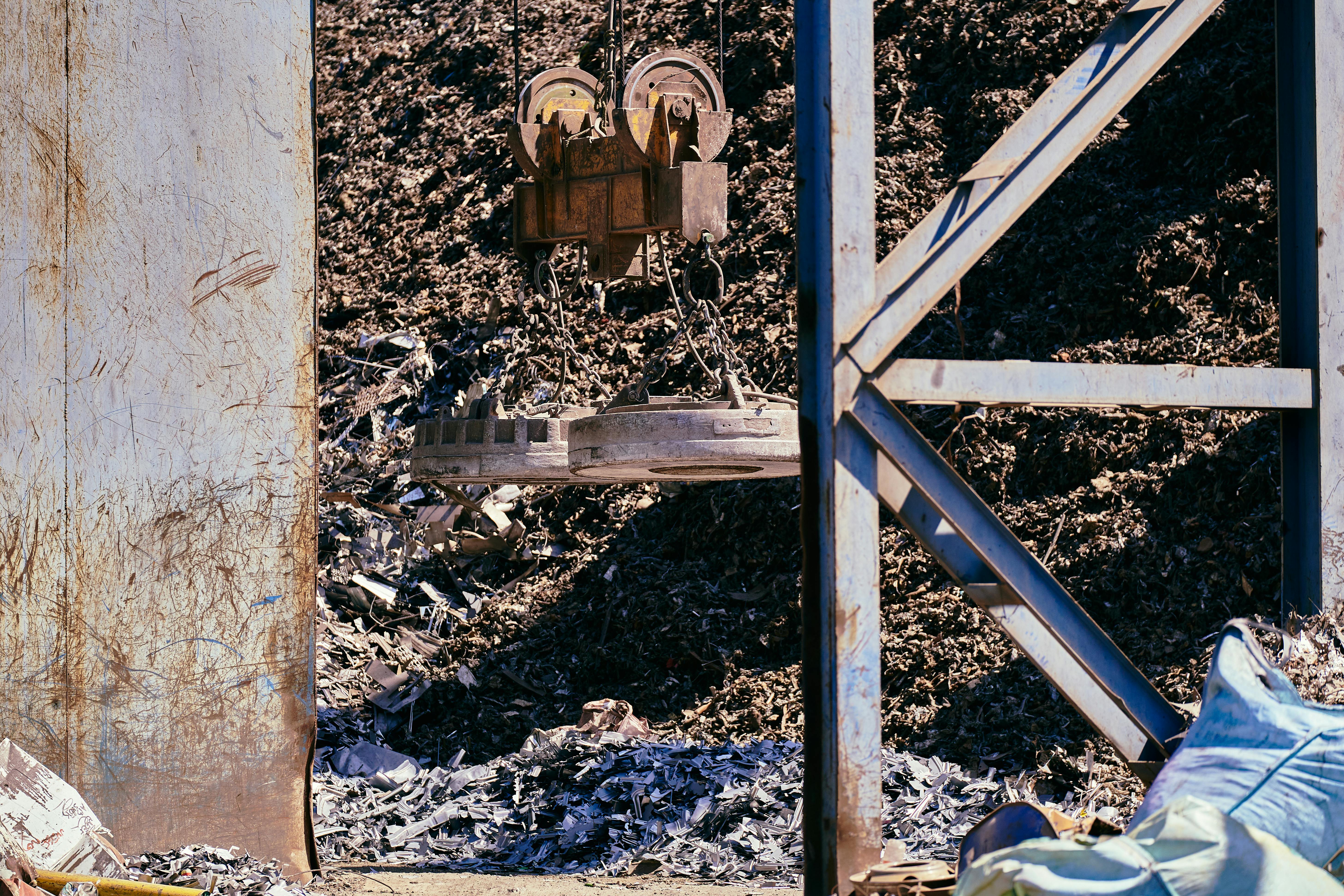 Free Magnetic crane sorting metal in an industrial scrapyard. Bright daylight highlights the steel and machinery. Stock Photo