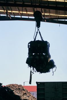 Silhouette of industrial crane lifting metal debris in a warehouse.