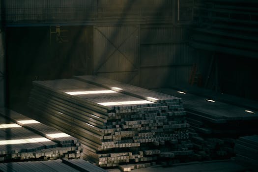Stacks of metal beams in a sunlit industrial warehouse interior.