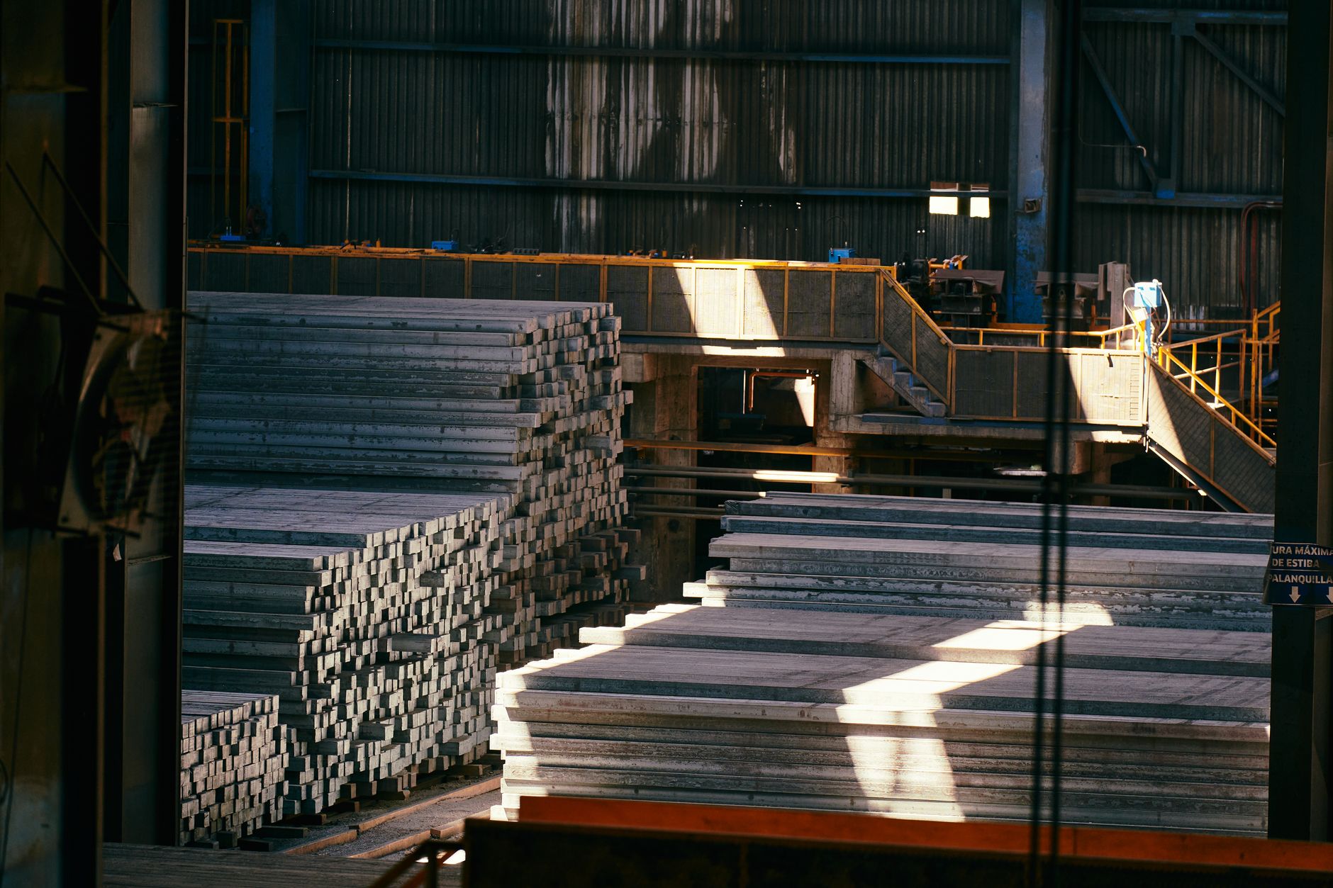 Interior view of a large industrial warehouse with stacked metal sheets and beams.