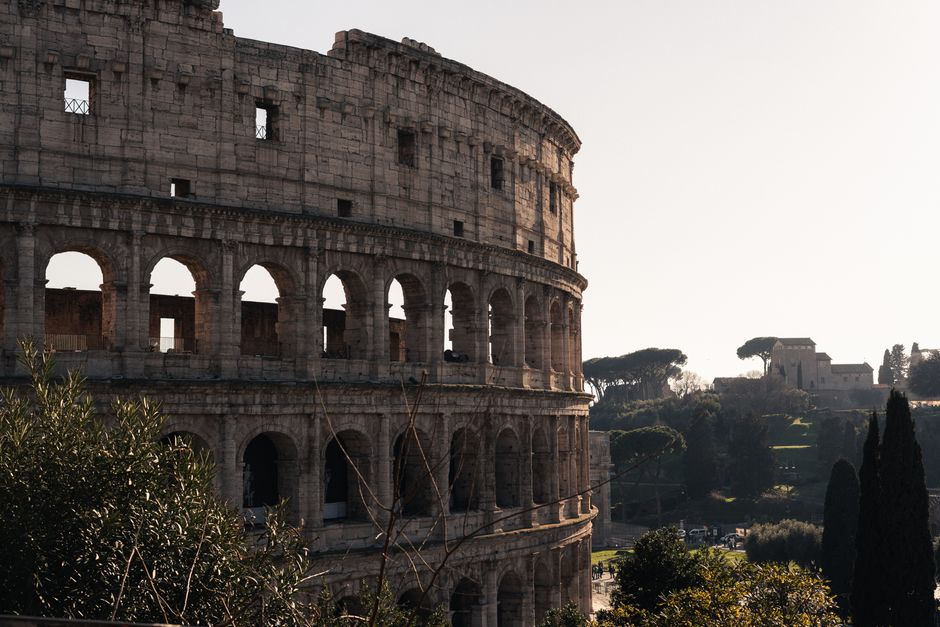 A warm daylight view of the iconic Colosseum in Rome, Italy, surrounded by greenery.