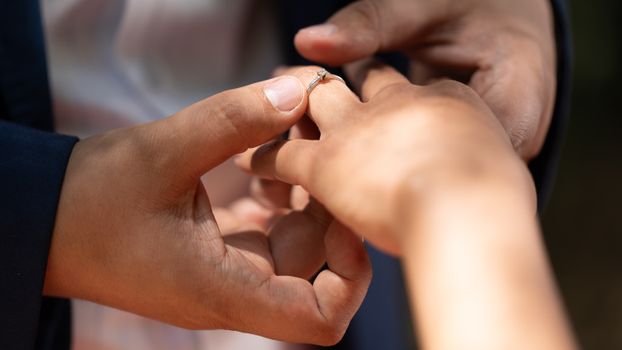 Close-up of an engagement ring being placed on a woman's hand in natural lighting.