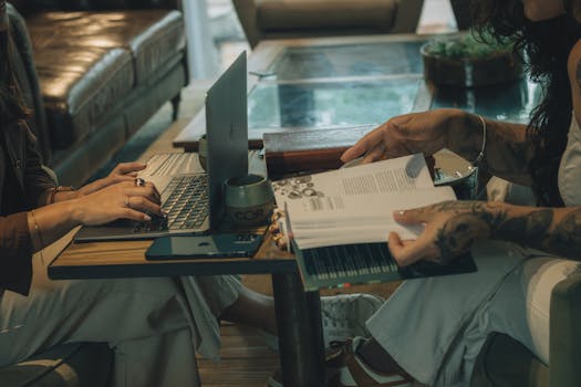 Two individuals engaging in work and study at a cozy indoor setting with laptop and book.