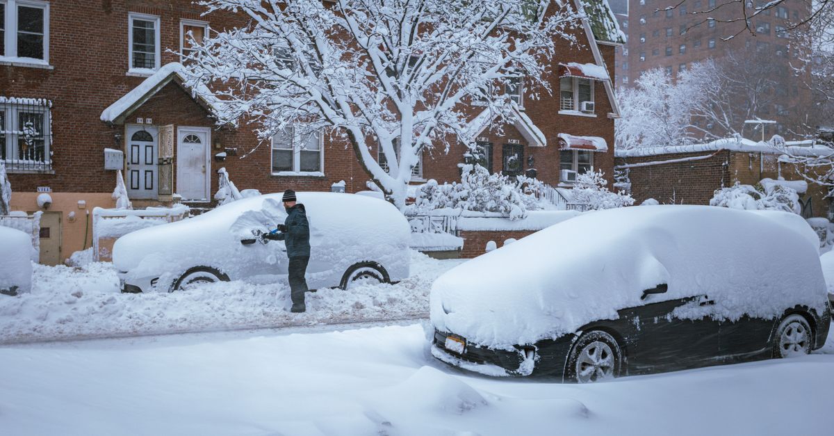 A person brushes snow off a car in a residential New York City neighborhood after a snowstorm.