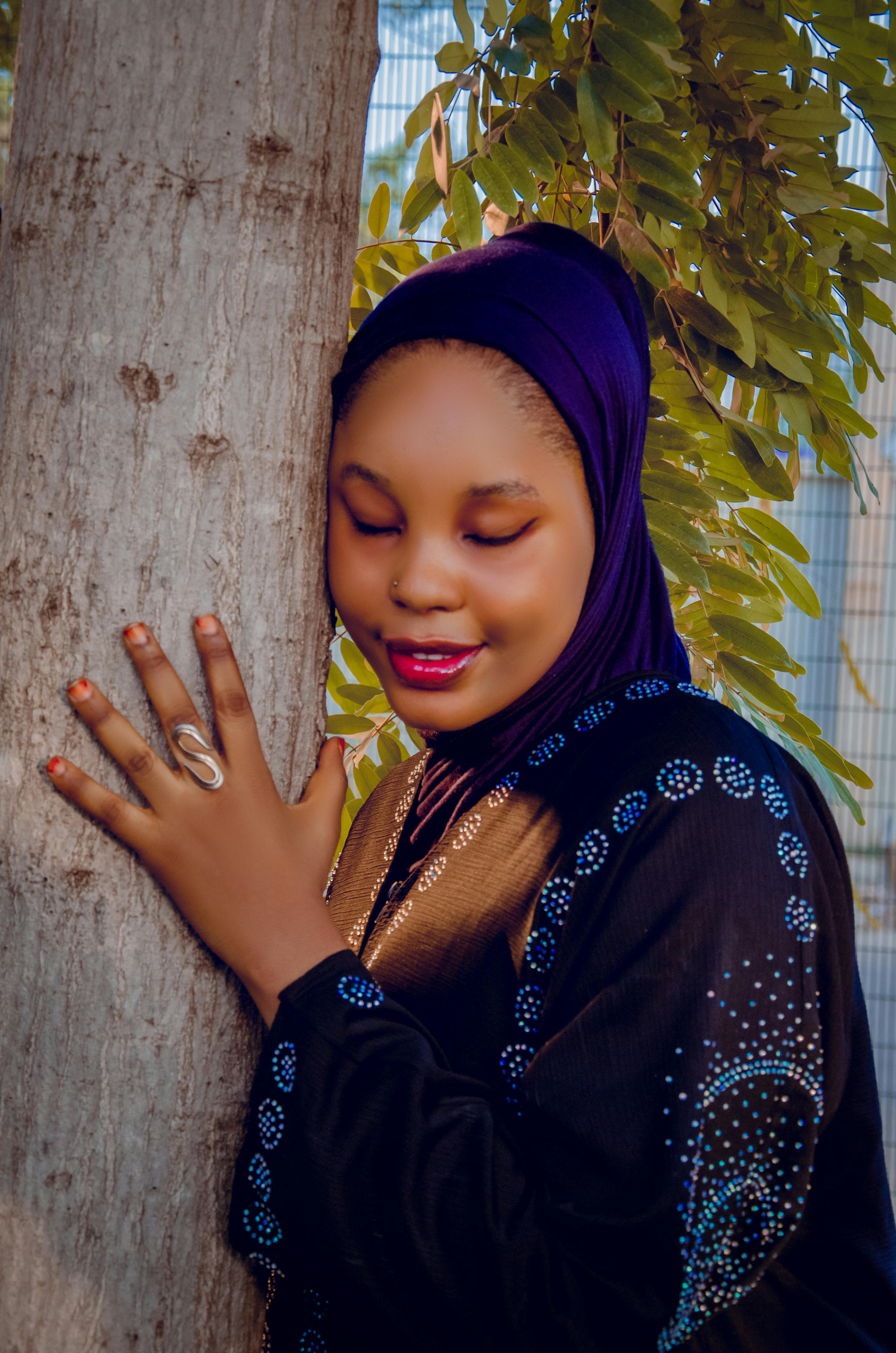 бесплатная Женщина в стильном хиджабе обнимает дерево, демонстрируя связь с природой. Стоковое фото