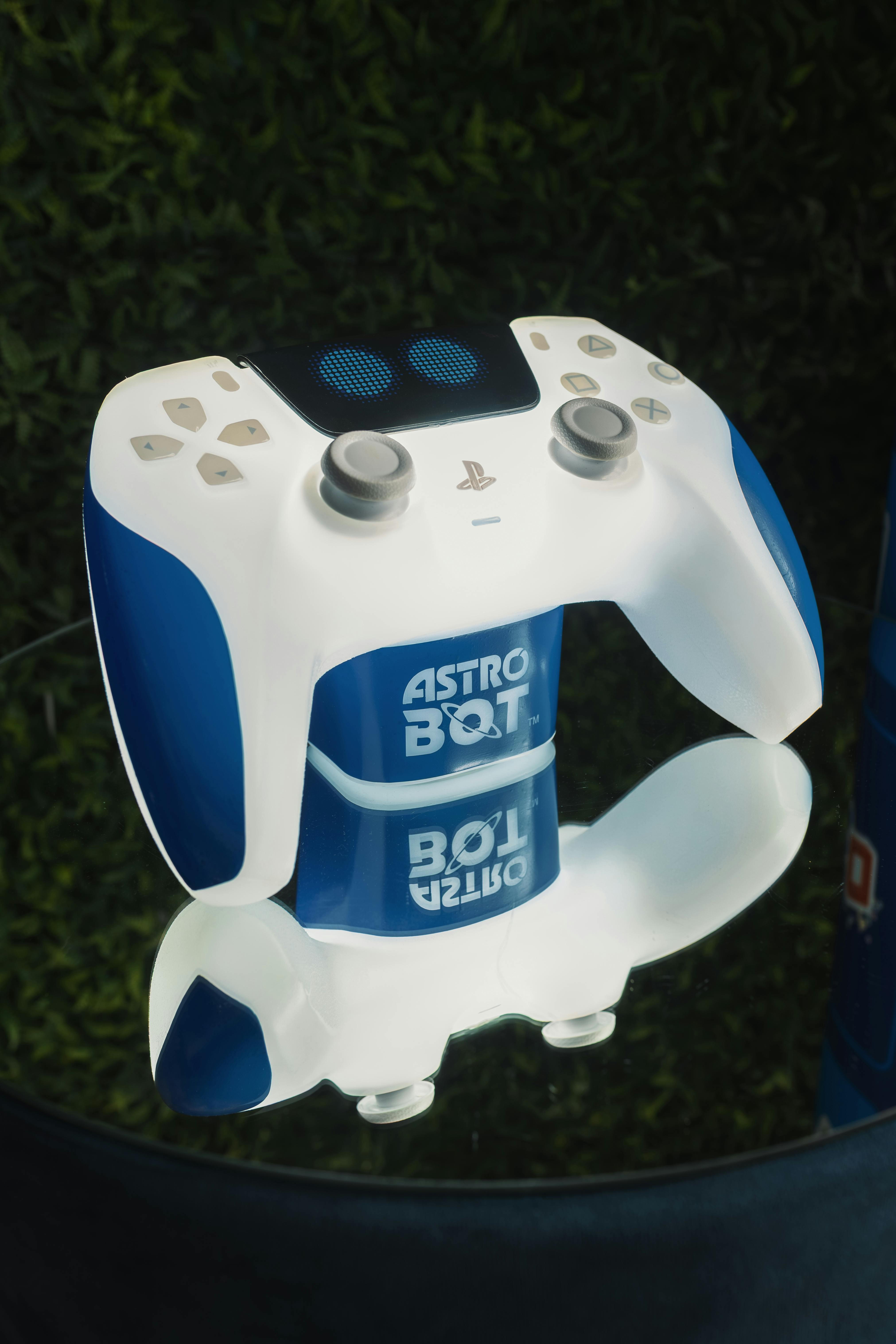 бесплатная Игровой контроллер сине-белого цвета с логотипом «Astro Bot» на отражающей поверхности. Стоковое фото