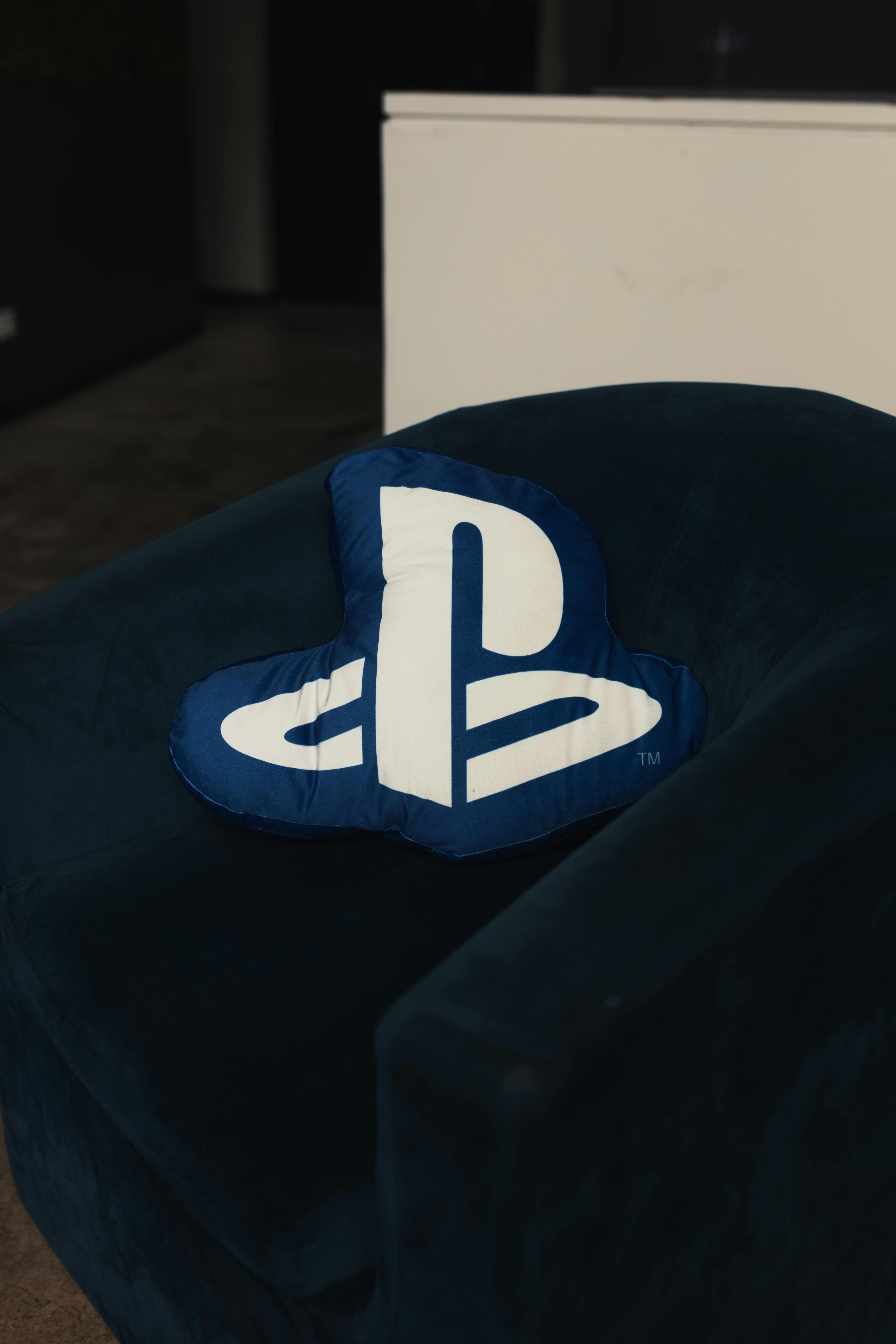 Δωρεάν Ένα μπλε μαξιλάρι με το λογότυπο του PlayStation τοποθετημένο σε μια σκούρα βελούδινη πολυθρόνα σε εσωτερικό χώρο. Φωτογραφία από στοκ φωτογραφιών