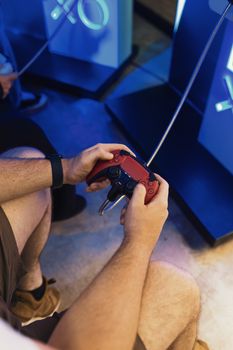 Close-up of a person holding a red gaming controller while playing on a console.