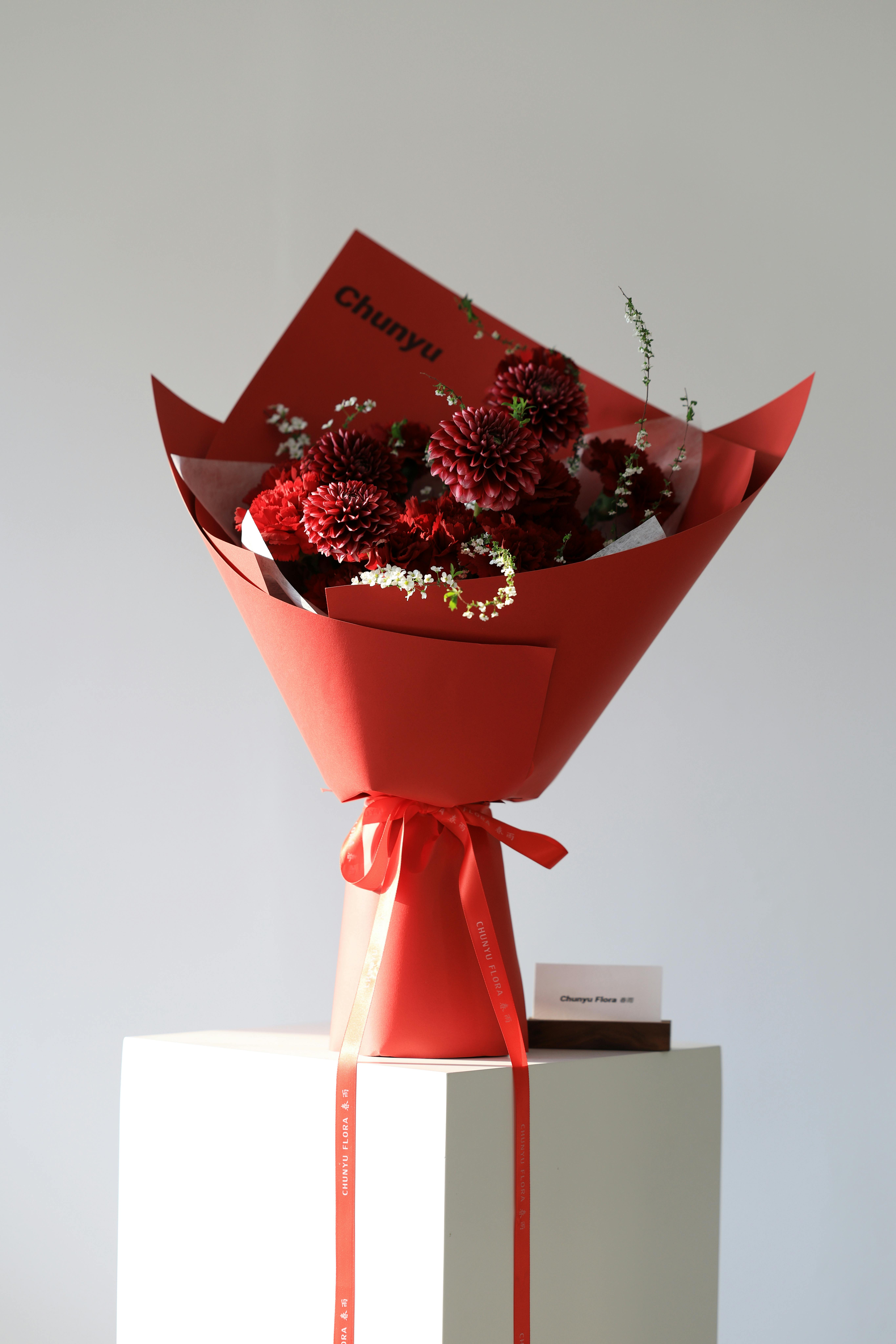 Free Elegant red dahlia bouquet wrapped in vibrant paper on display pedestal. Perfect for special occasions. Stock Photo