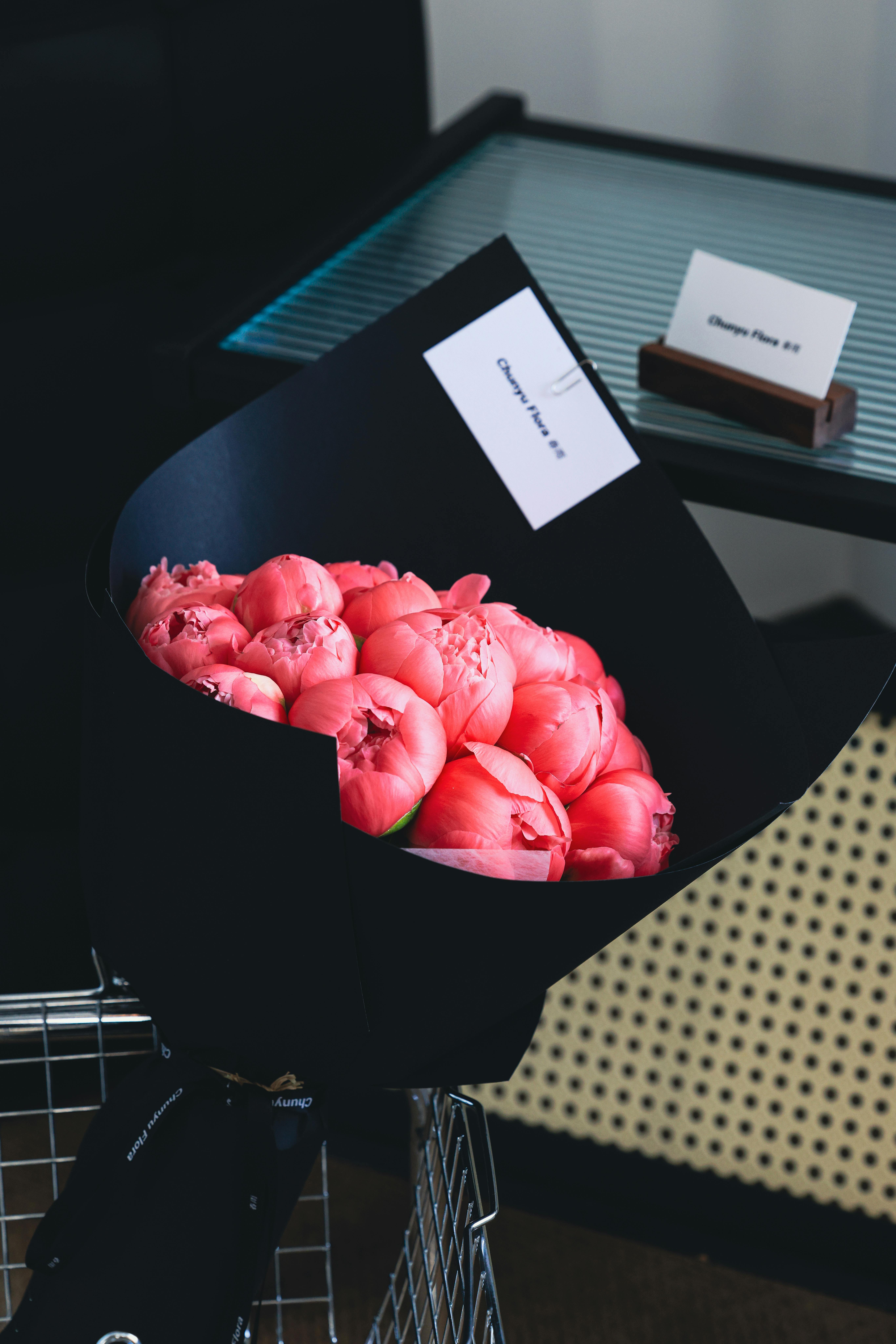 Gratis Un elegante bouquet di fiori rosa vivaci, avvolto in carta nera, esposto in modo creativo all'interno. Foto a disposizione