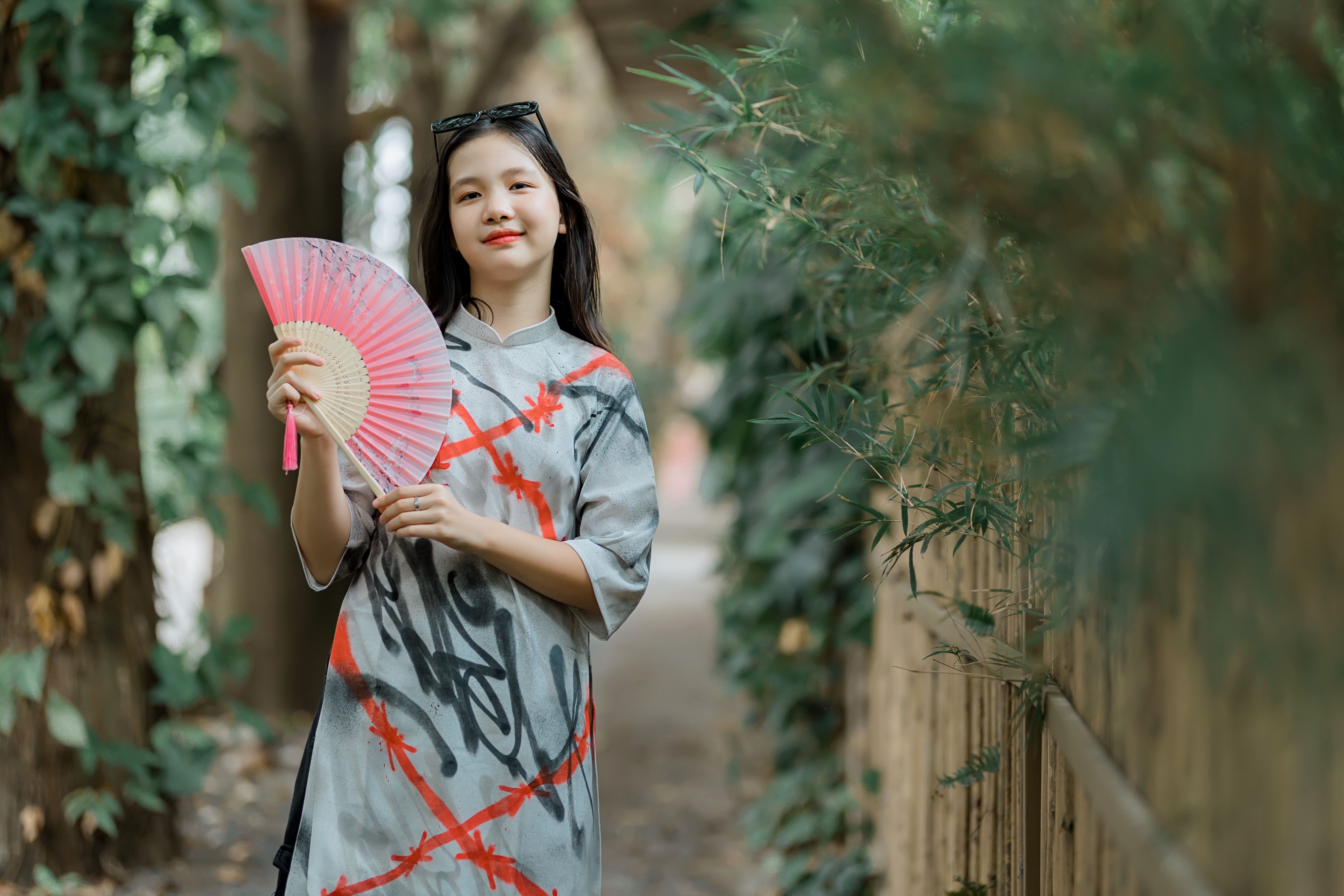Young woman in a colorful garment holding a bamboo hand fan, enjoying a peaceful outdoor setting.