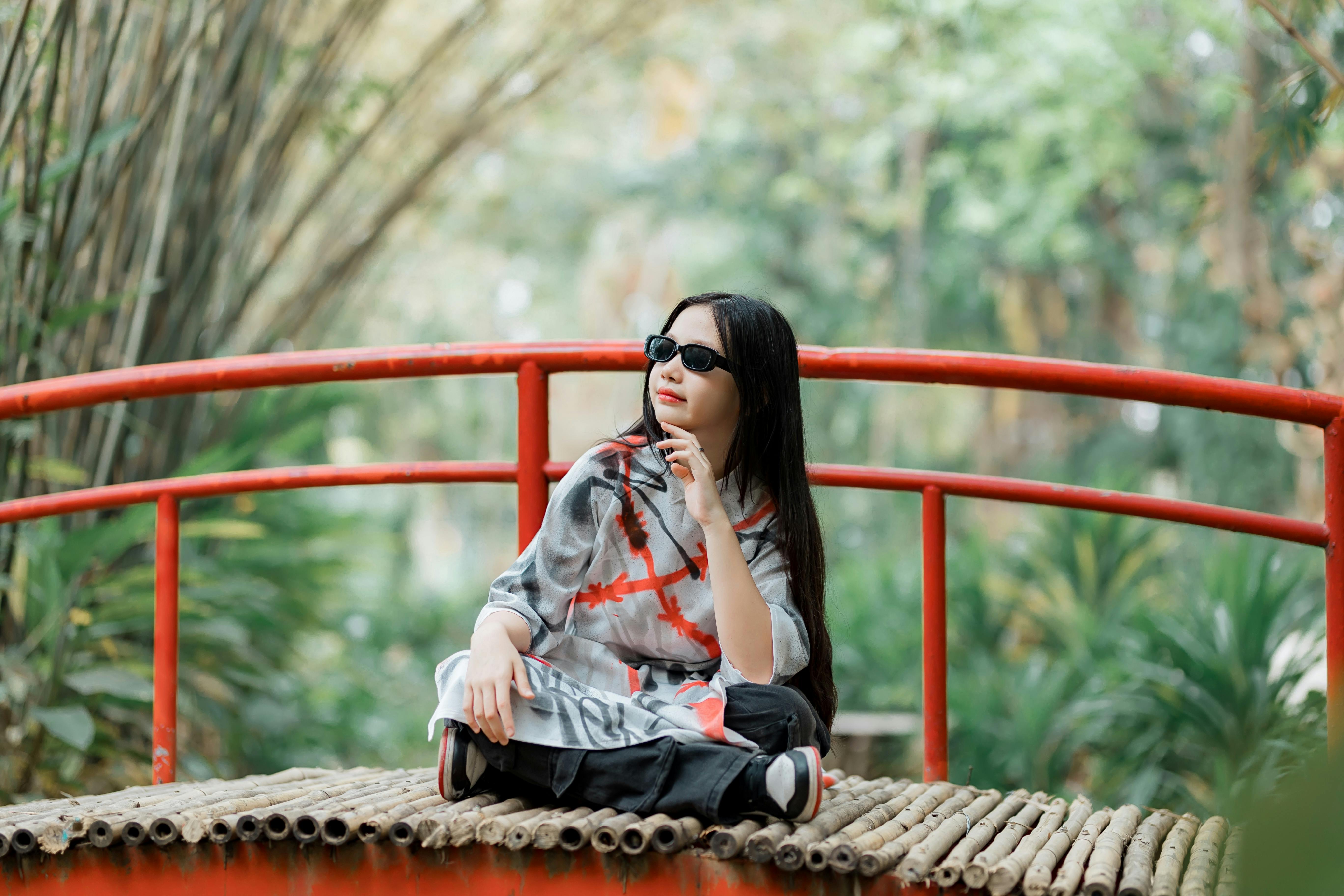 бесплатная Женщина в солнцезащитных очках наслаждается безмятежным моментом на бамбуковом мосту на открытом воздухе. Стоковое фото