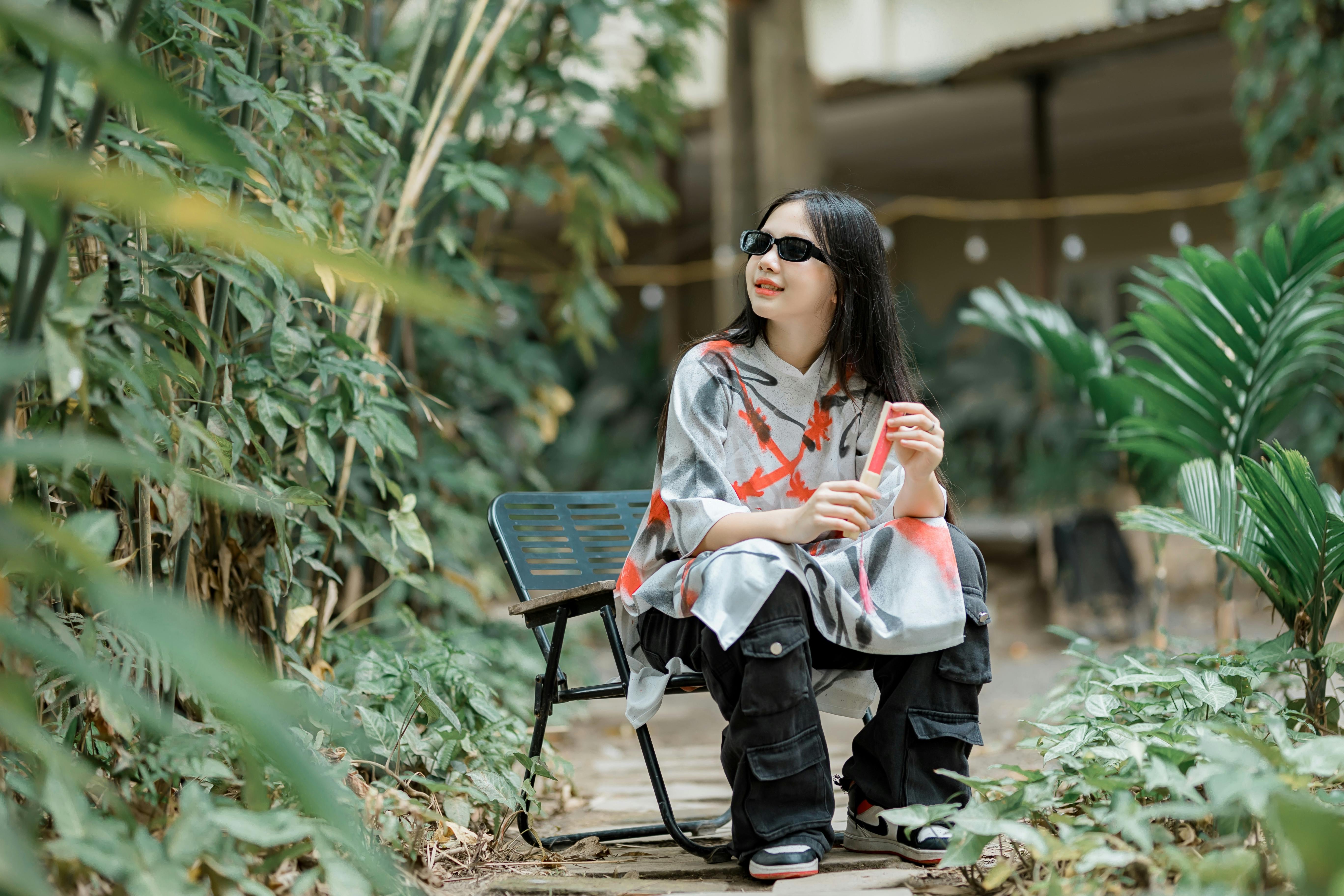 бесплатная Молодая женщина сидит в пышном тропическом саду, наслаждаясь солнечным днем. Стоковое фото