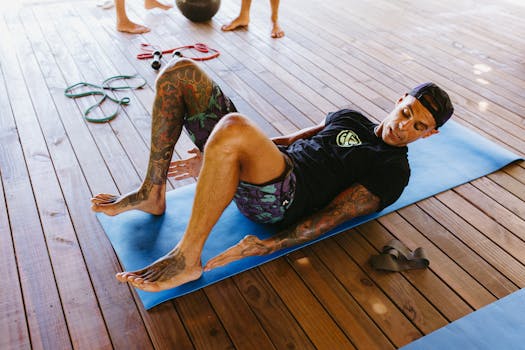 Tattooed man exercising outdoors on a mat, using CrossFit equipment on a wooden deck.