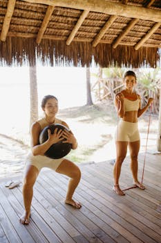 Two women engaged in an outdoor workout, performing functional fitness exercises with equipment.