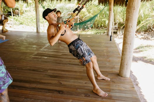 Fit man performing TRX workout on a wooden deck with tropical backdrop, showcasing outdoor exercise and healthy lifestyle.